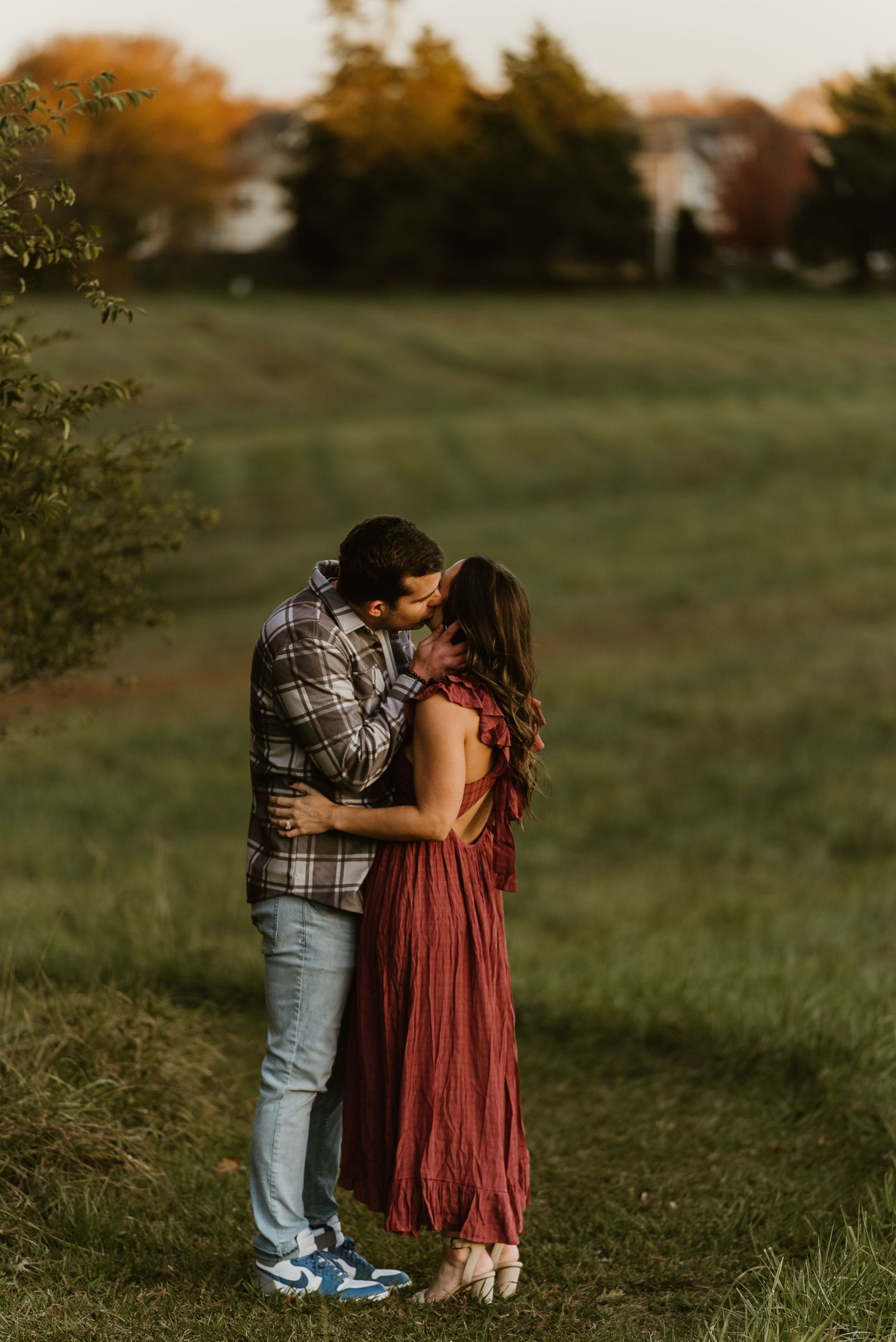 Couple sharing a romantic kiss in an open green field during a warm golden sunset engagement session.