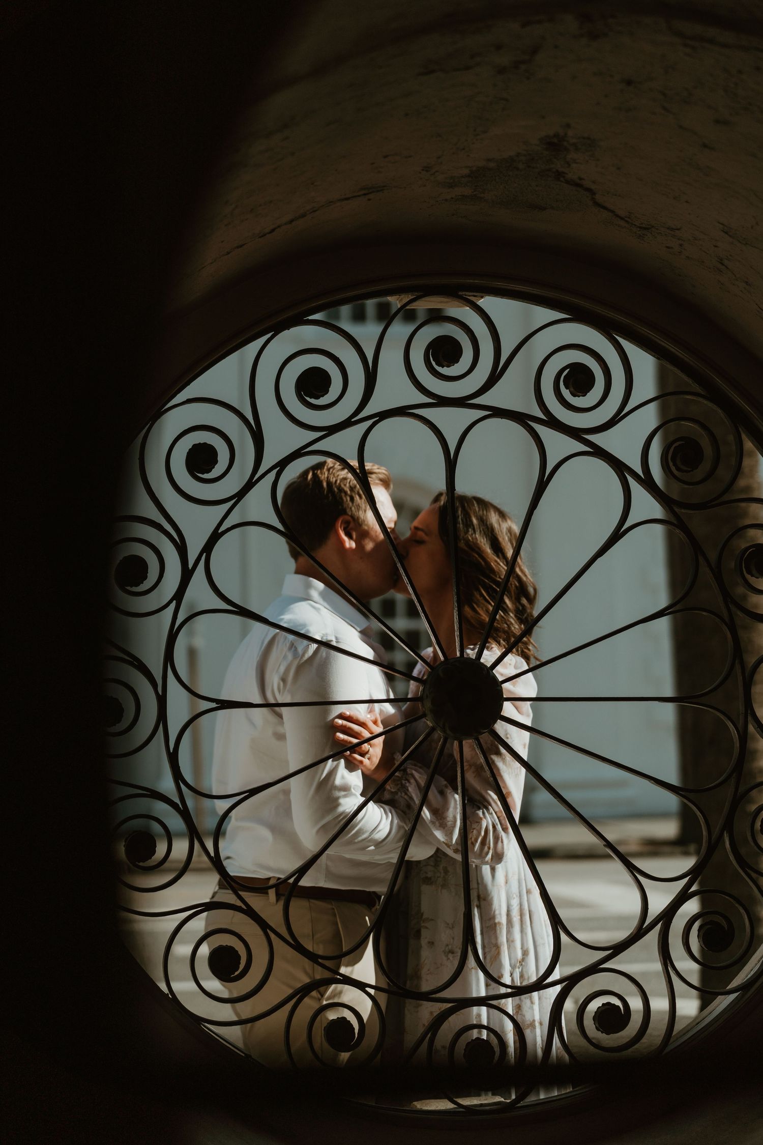 Romantic couple kissing viewed through an ornate circular wrought iron gate in a dreamy artistic composition.