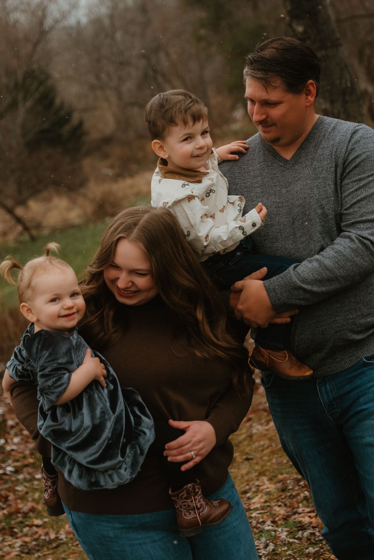 Smiling family of four with two young children enjoying a casual outdoor winter photo session.