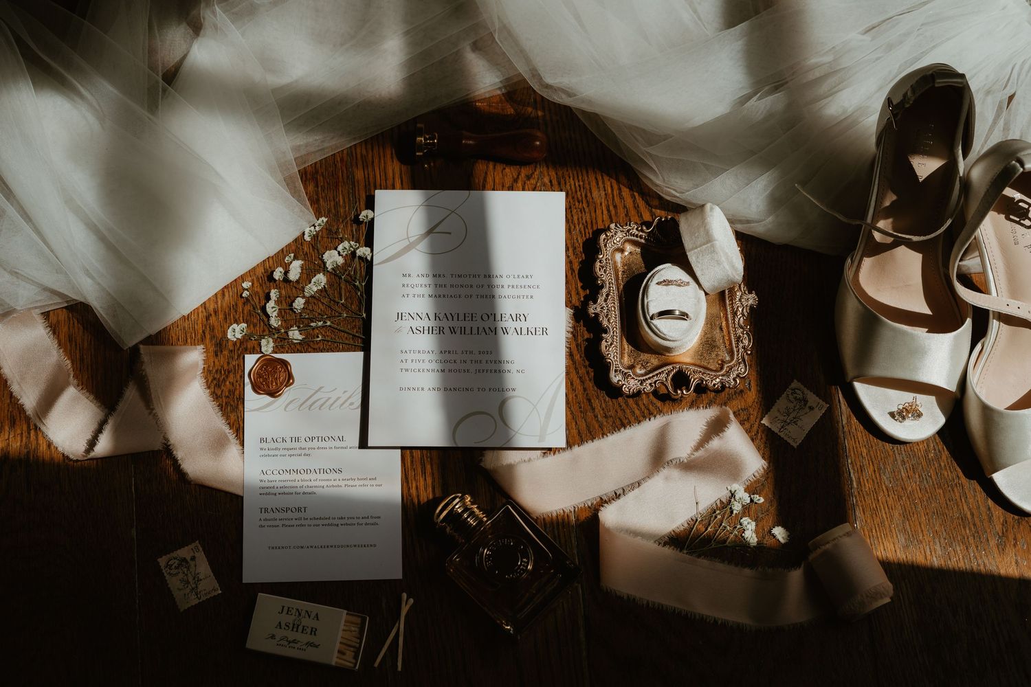 Elegant wedding flat lay featuring invitations, wax seal, rings, ribbon, and bridal heels on wood.
