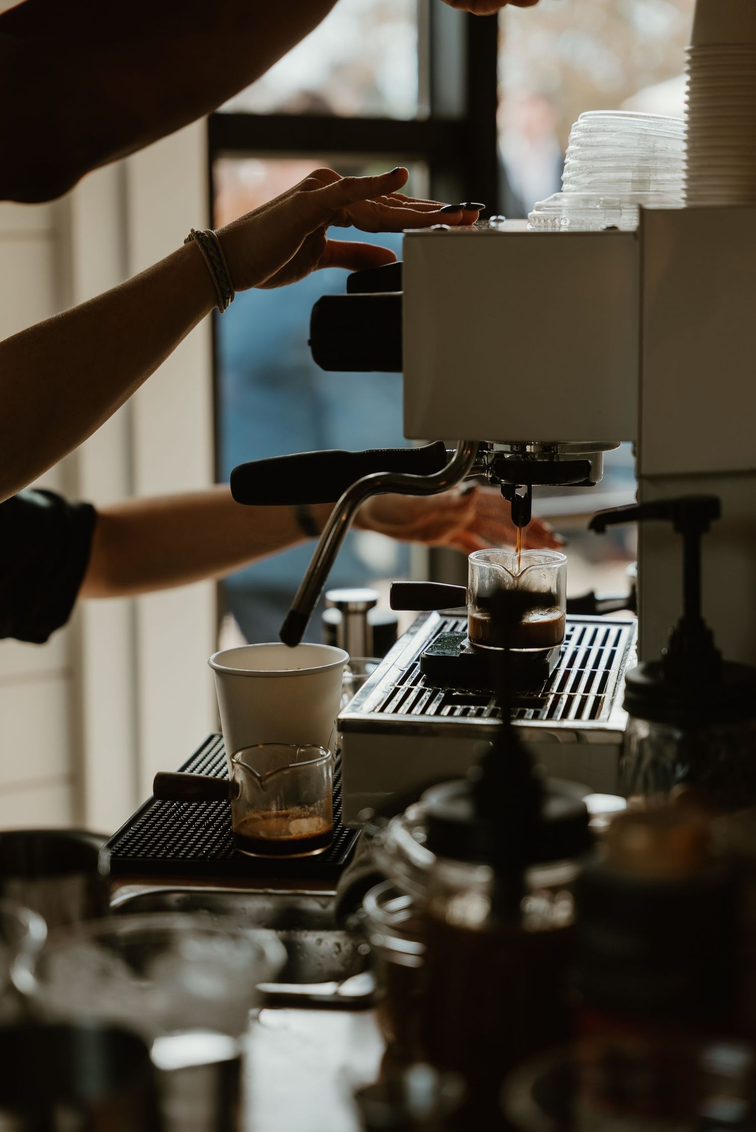 Barista operating espresso machine pouring fresh coffee at a cafe counter with cups nearby.