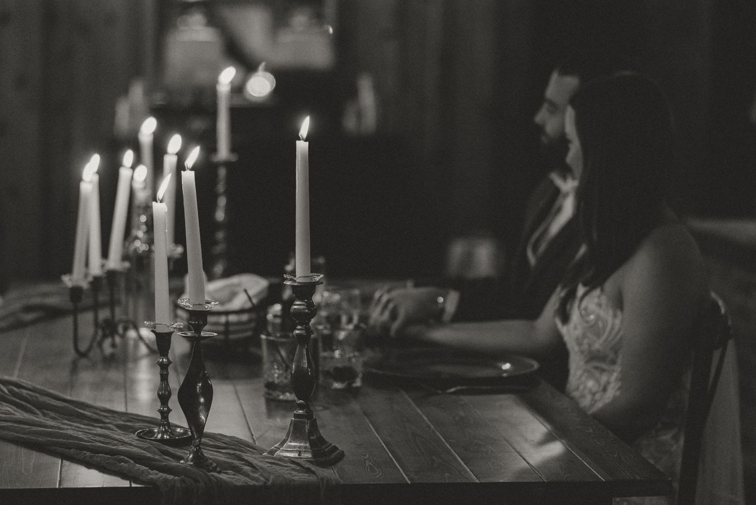Black and white photo of a woman sitting at a candlelit table with elegant candelabras in dim light.
