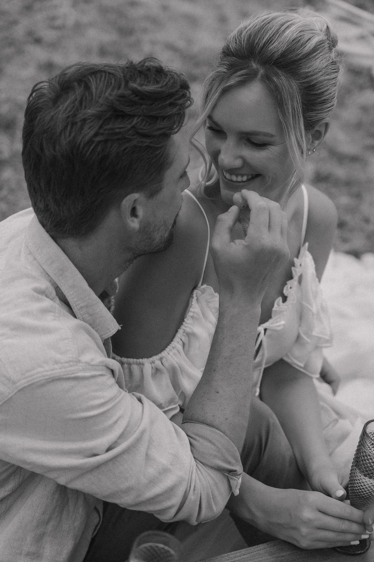 Black and white photo of a laughing couple sharing an intimate moment during an outdoor picnic.