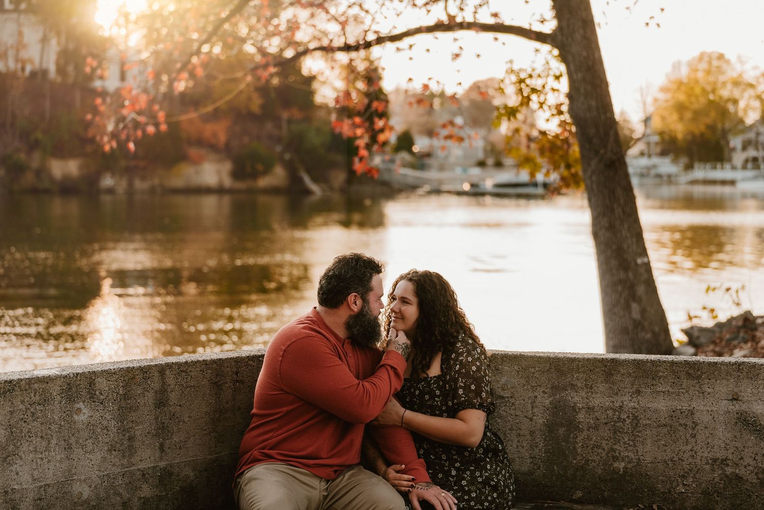 Couple sitting together by a sunlit lake sharing an intimate moment in fall.