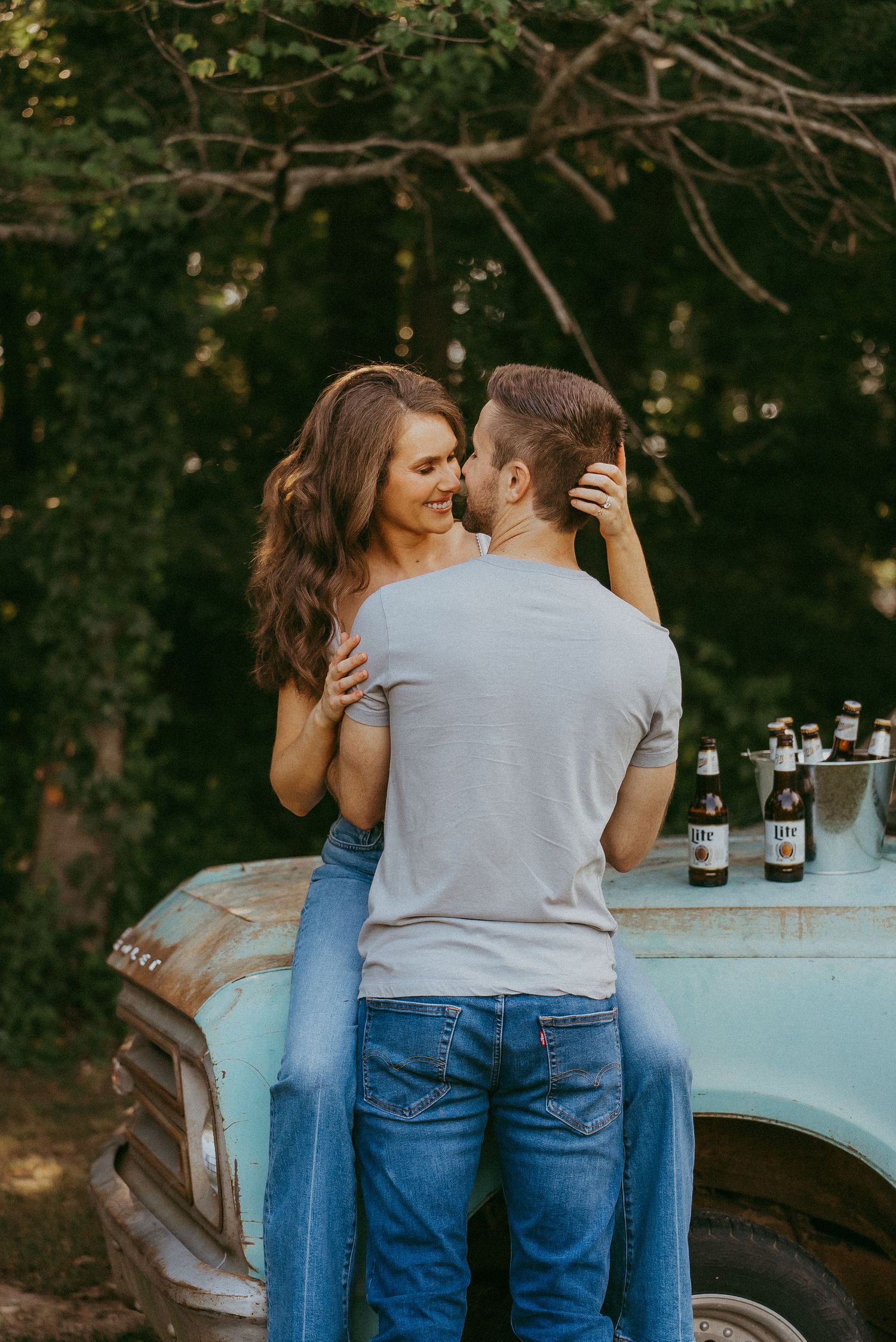 Couple sharing a tender embrace near a vintage turquoise truck with beer bottles on the hood.