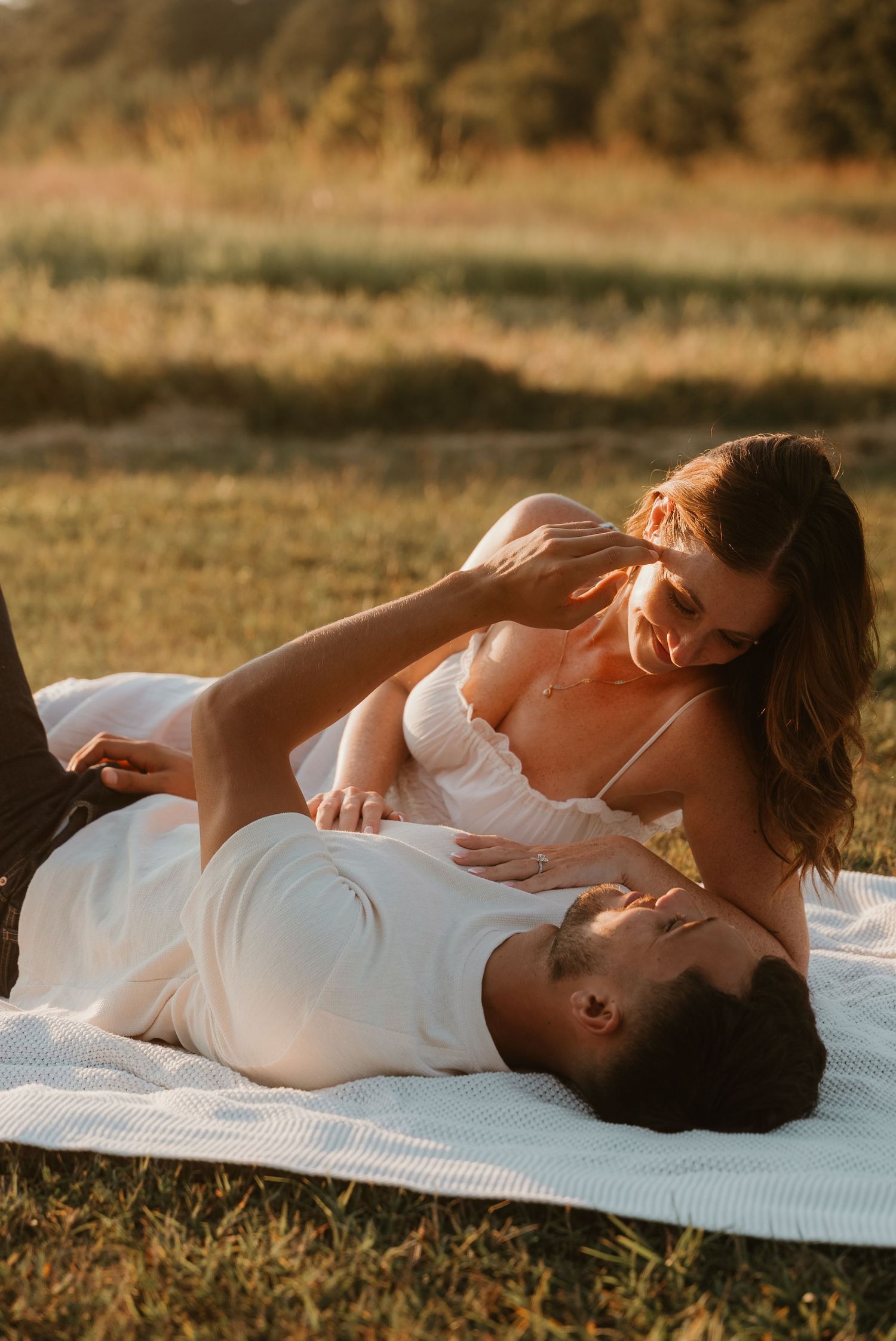 Couple sharing a playful intimate moment on a white blanket during outdoor golden hour session.