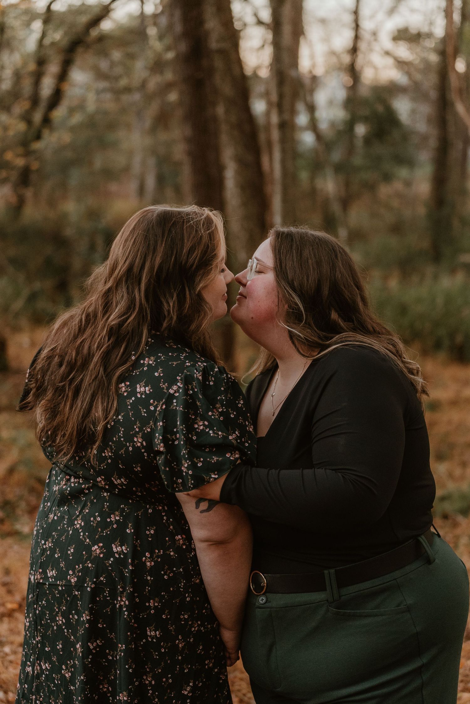 Two women sharing a romantic kiss in an autumn forest setting.