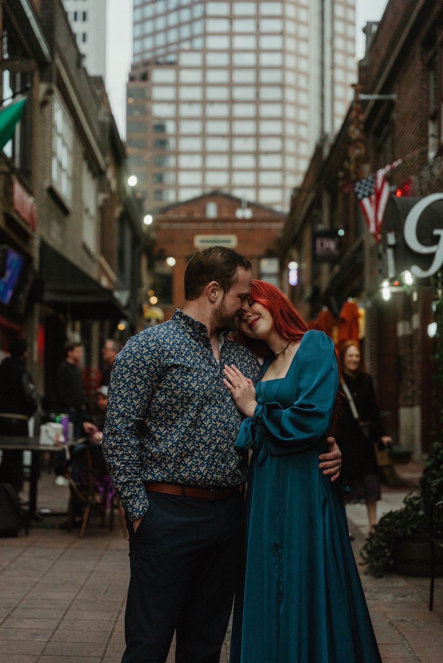 Couple sharing a romantic moment in a city alley, woman in teal dress and man in floral shirt.