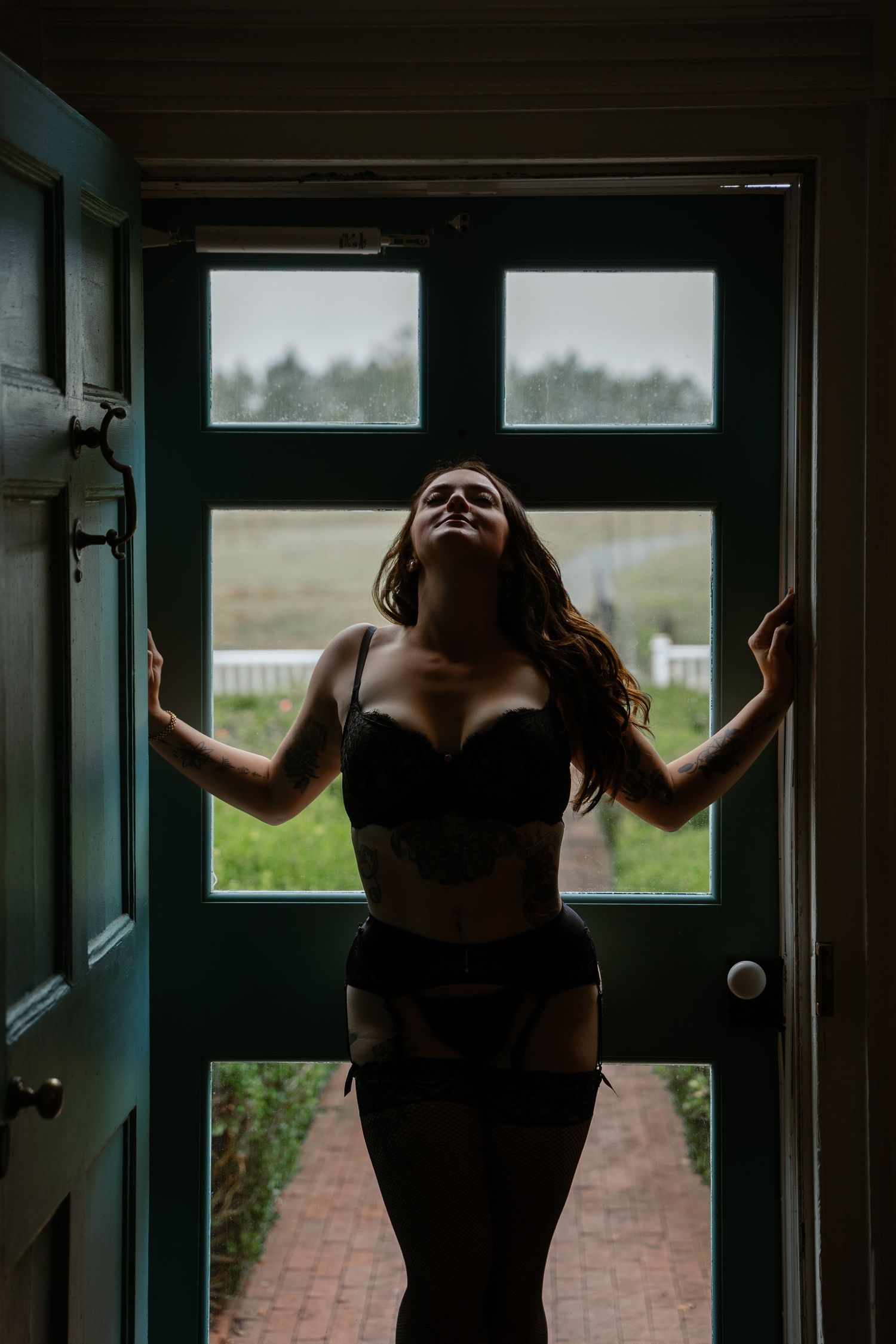 Silhouette of woman in black lingerie standing in doorway with outdoor light behind.