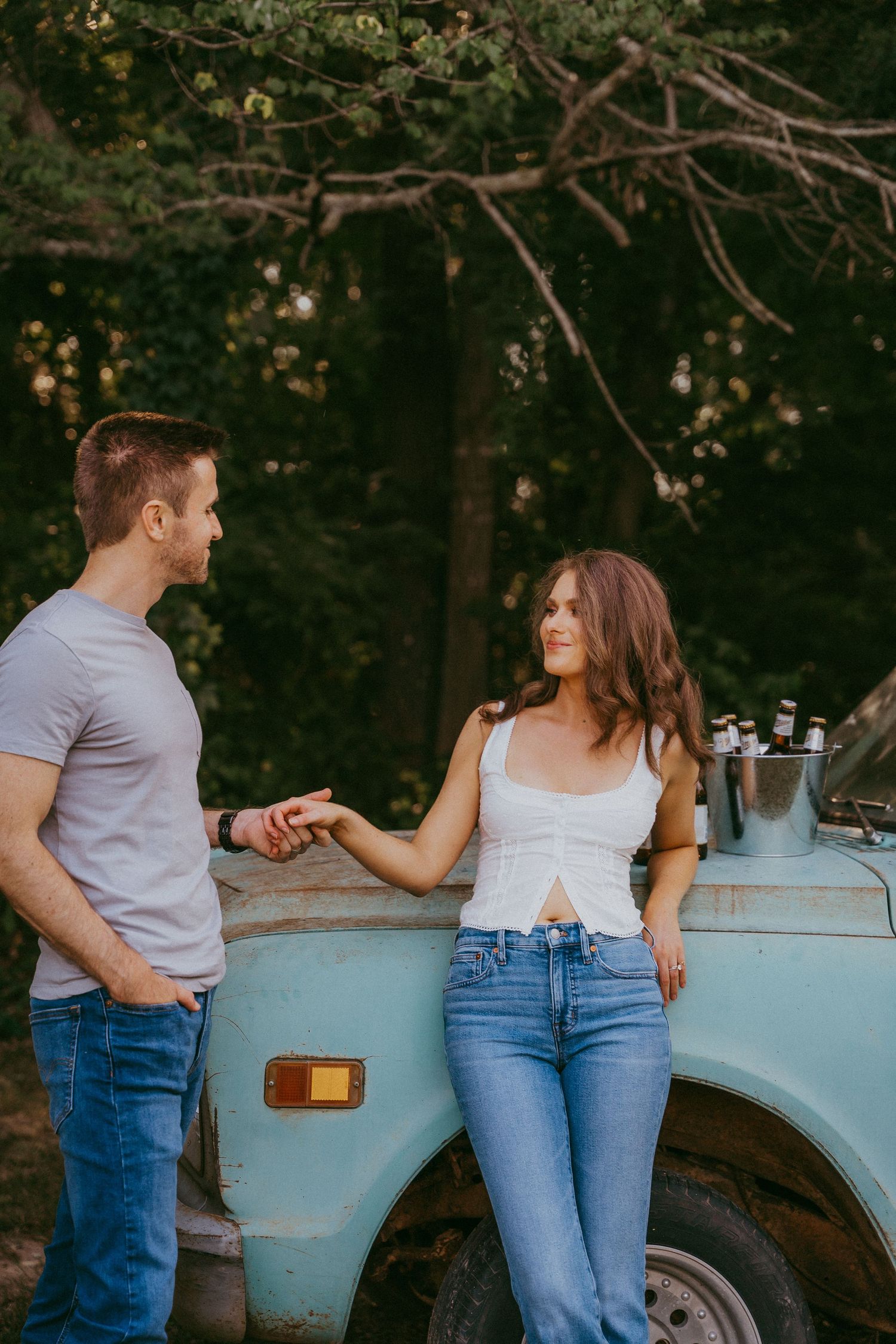 Couple holding hands and gazing at each other beside a vintage light blue truck.