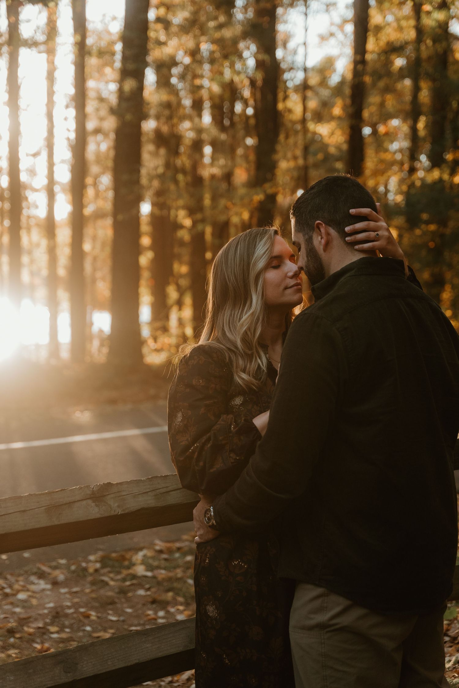 Couple sharing an intimate embrace in a sunlit autumn forest with golden rays filtering through trees.