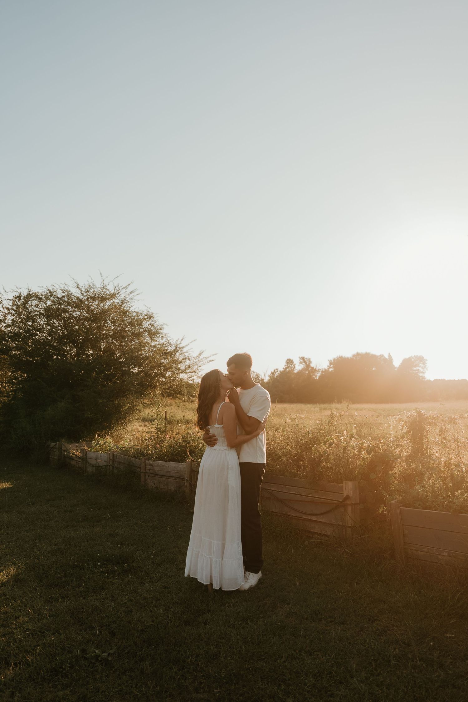 Couple kissing tenderly in an open field bathed in warm golden hour sunset light.