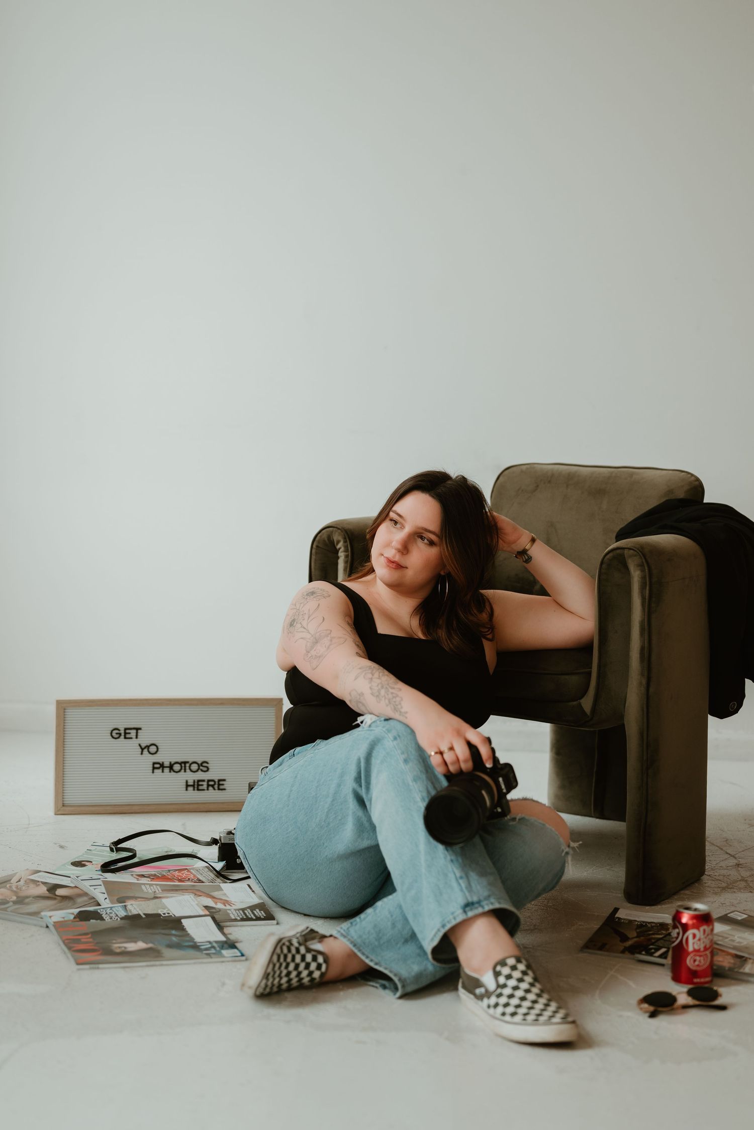 Young woman photographer sitting on floor with camera next to a letterboard sign.