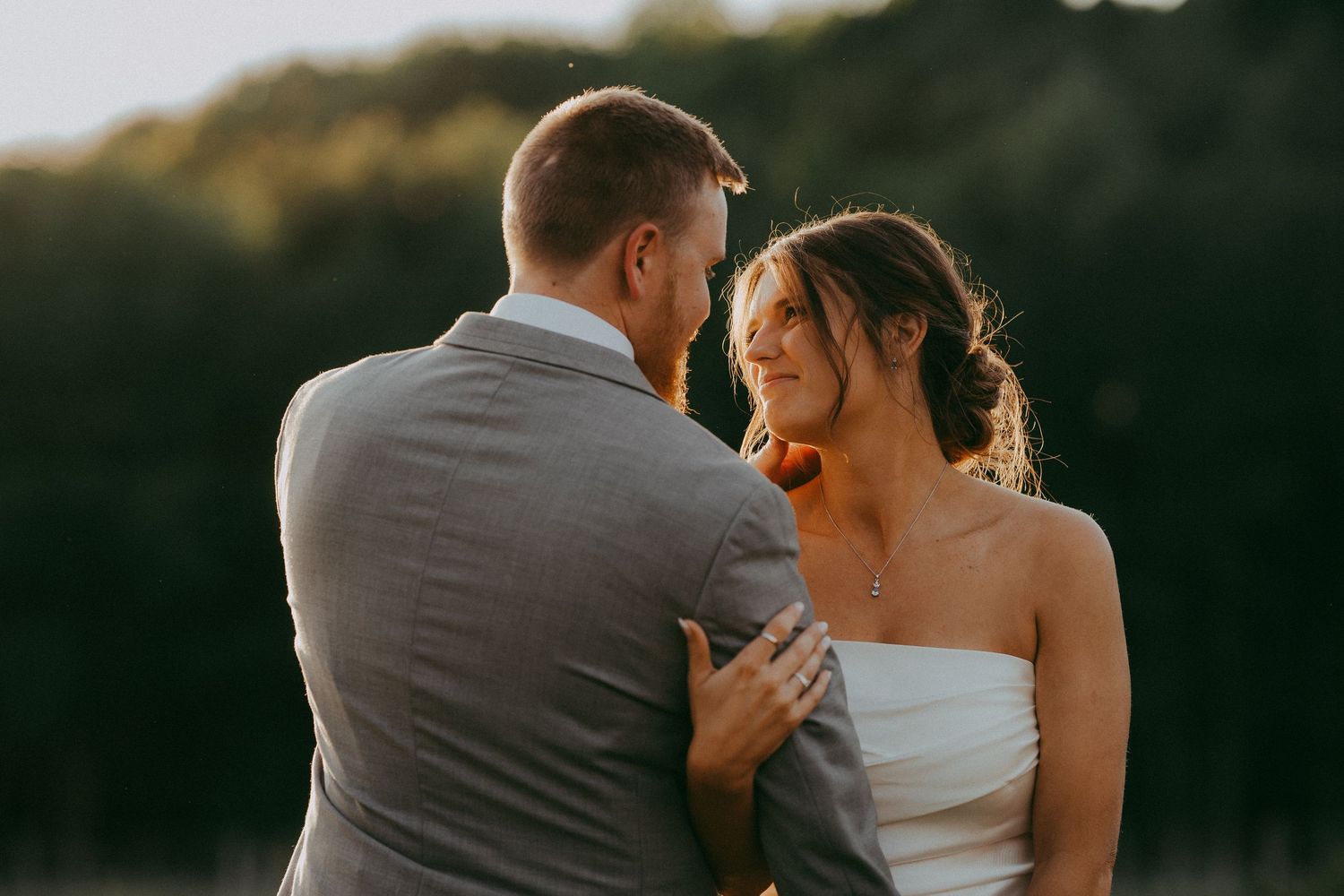 Bride and groom sharing a tender moment outdoors in warm golden sunset light at their wedding.