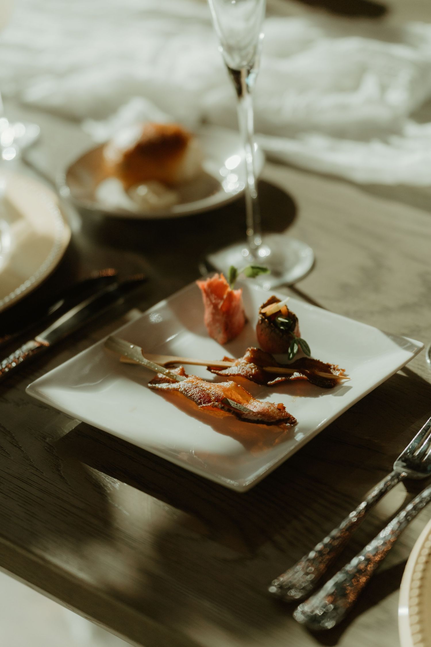 Elegant wedding reception plate with duck or salmon appetizer beside champagne flute and cutlery.