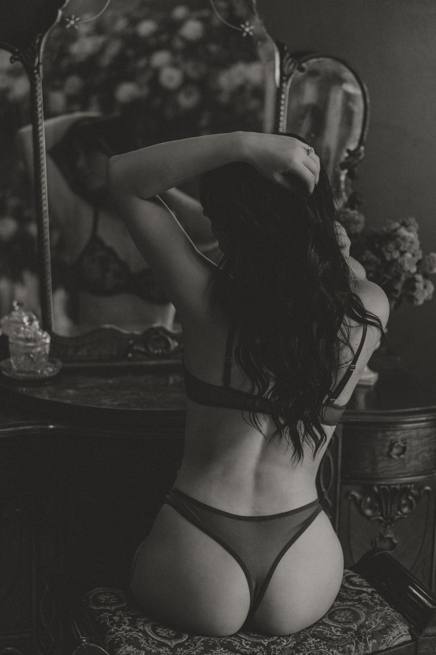 Black and white photo of a woman in lingerie kneeling before a vintage mirror with long flowing hair.