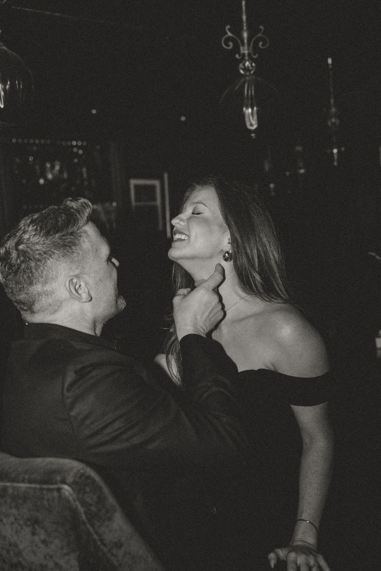 Black and white photo of a couple laughing together in a dimly lit elegant venue.