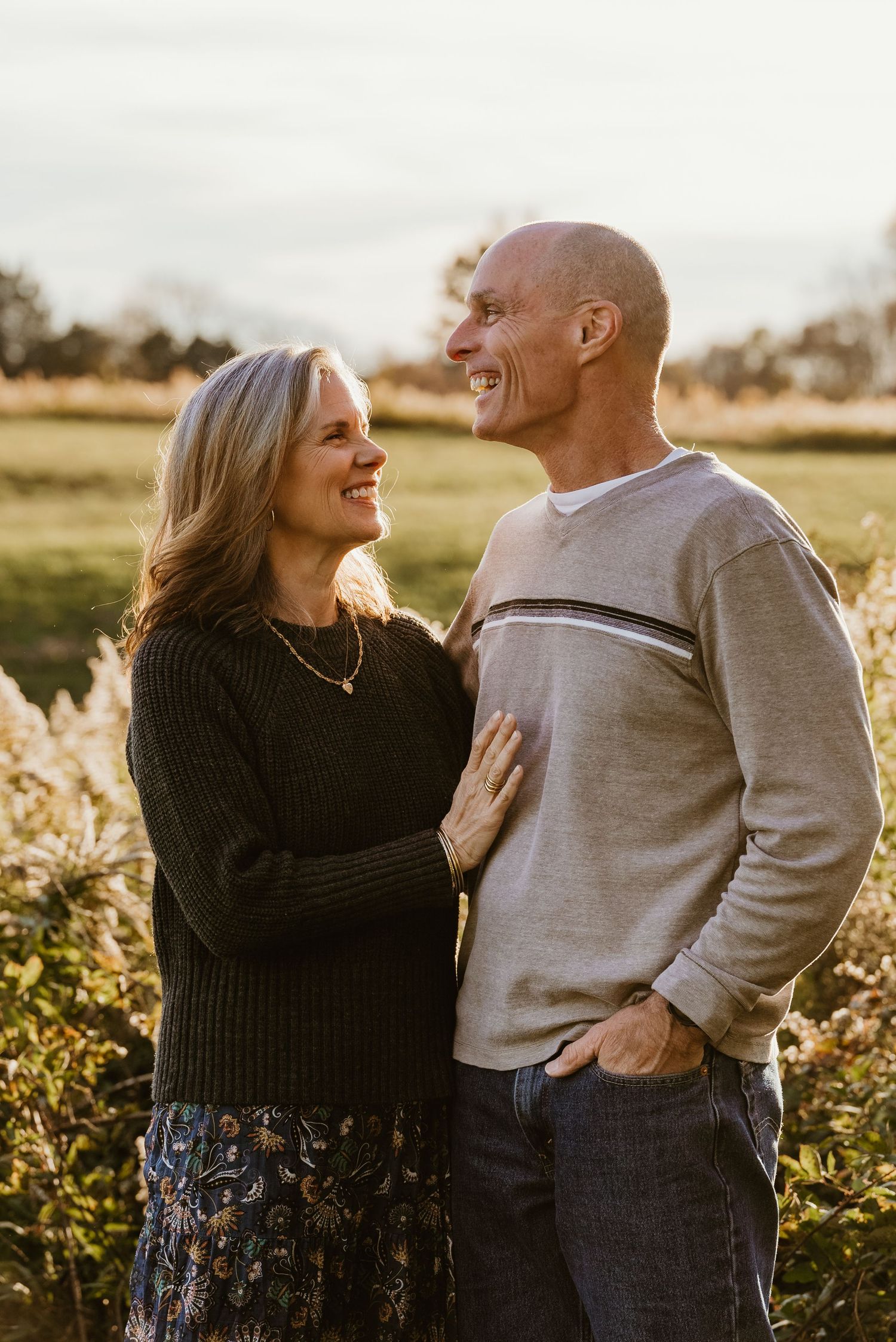 Happy couple laughing together in a sunlit autumn field, woman placing hand on mans chest.