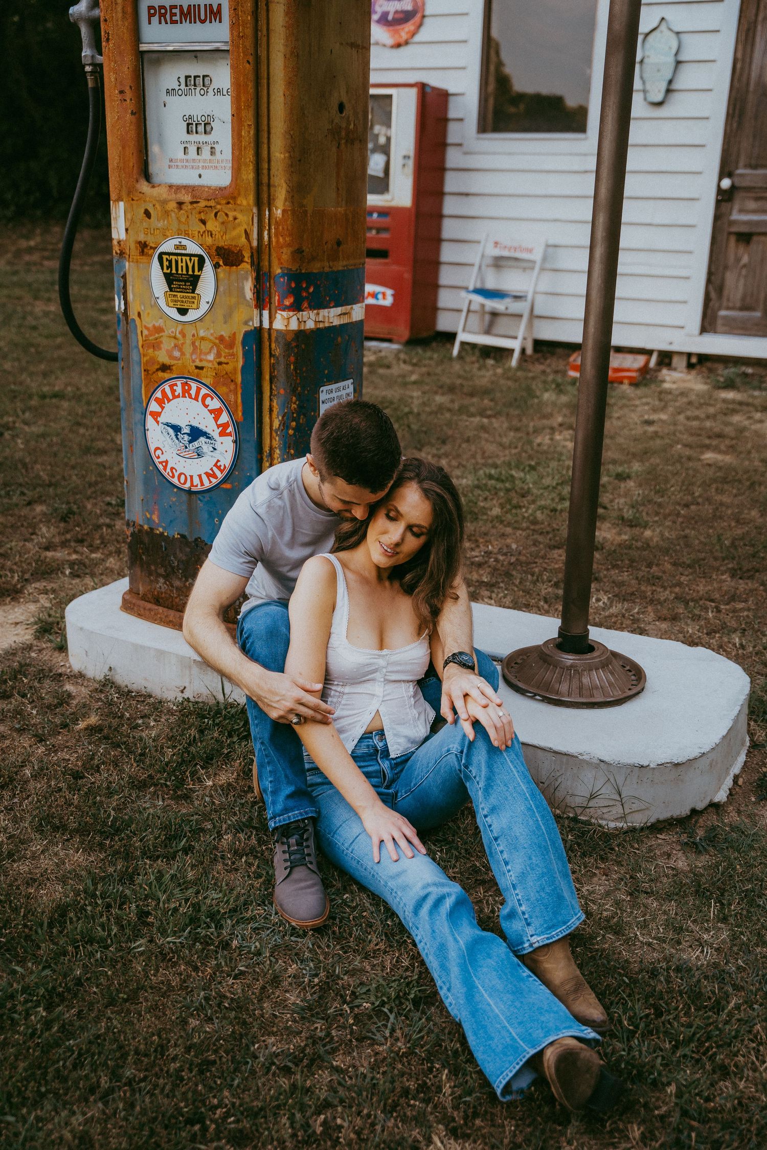 Couple sitting together at an old American Gasoline premium fuel pump during an engagement shoot.