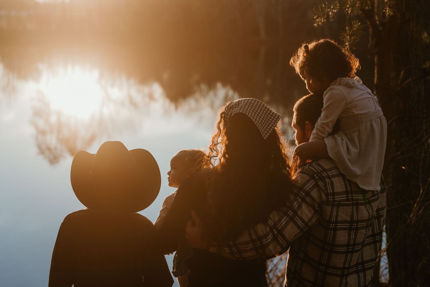 Family silhouetted against a glowing sunset by a lake, sharing a warm embrace outdoors.