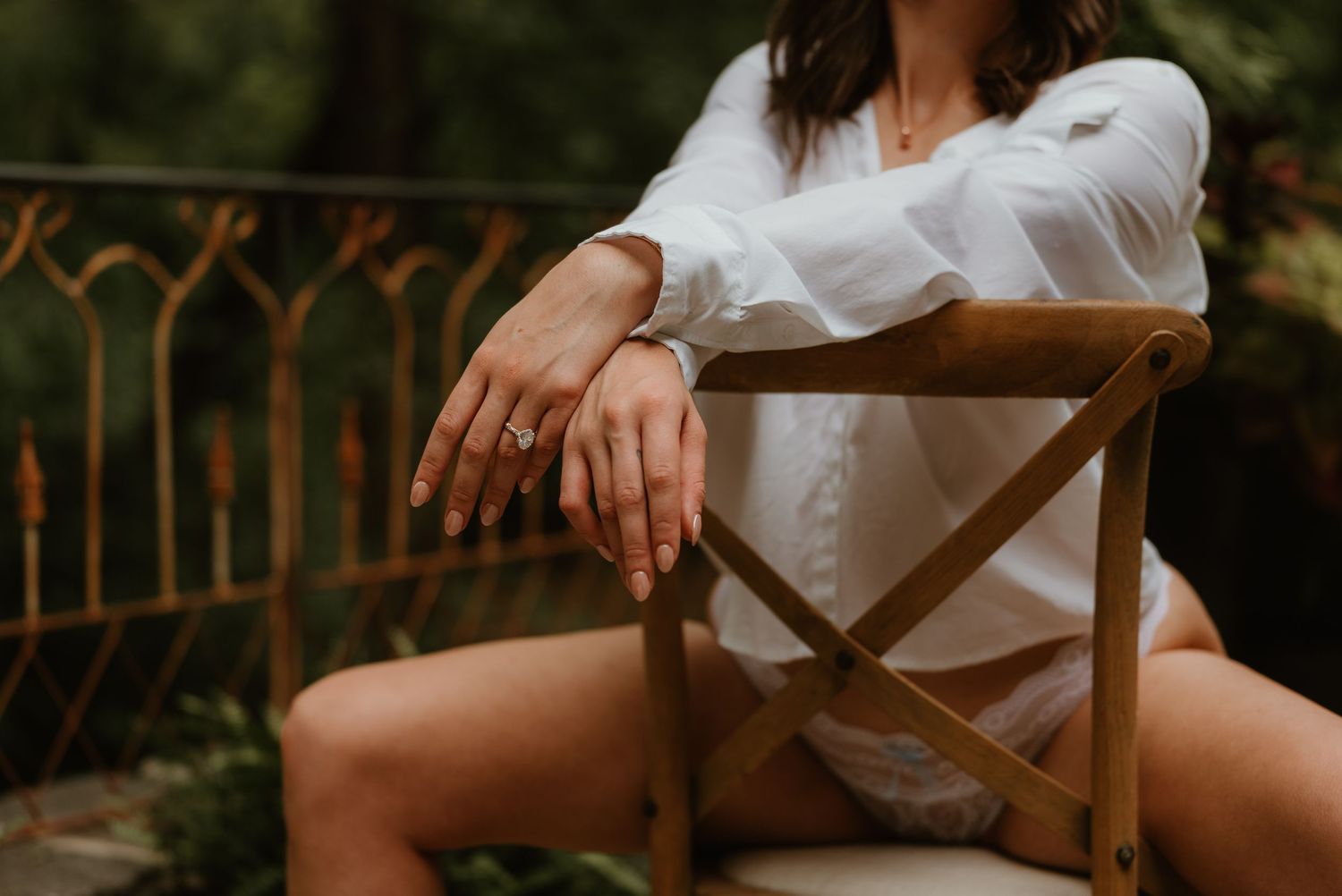 Woman in white shirt and lingerie posing gracefully on wooden chair outdoors.