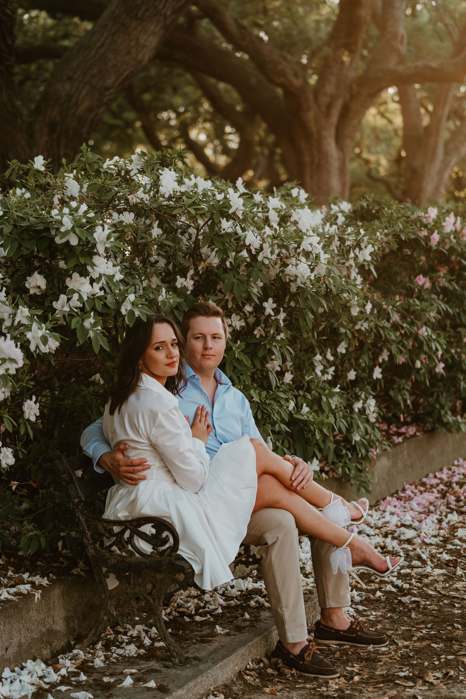 Couple sitting on a bench surrounded by blooming white flowers in golden hour light.