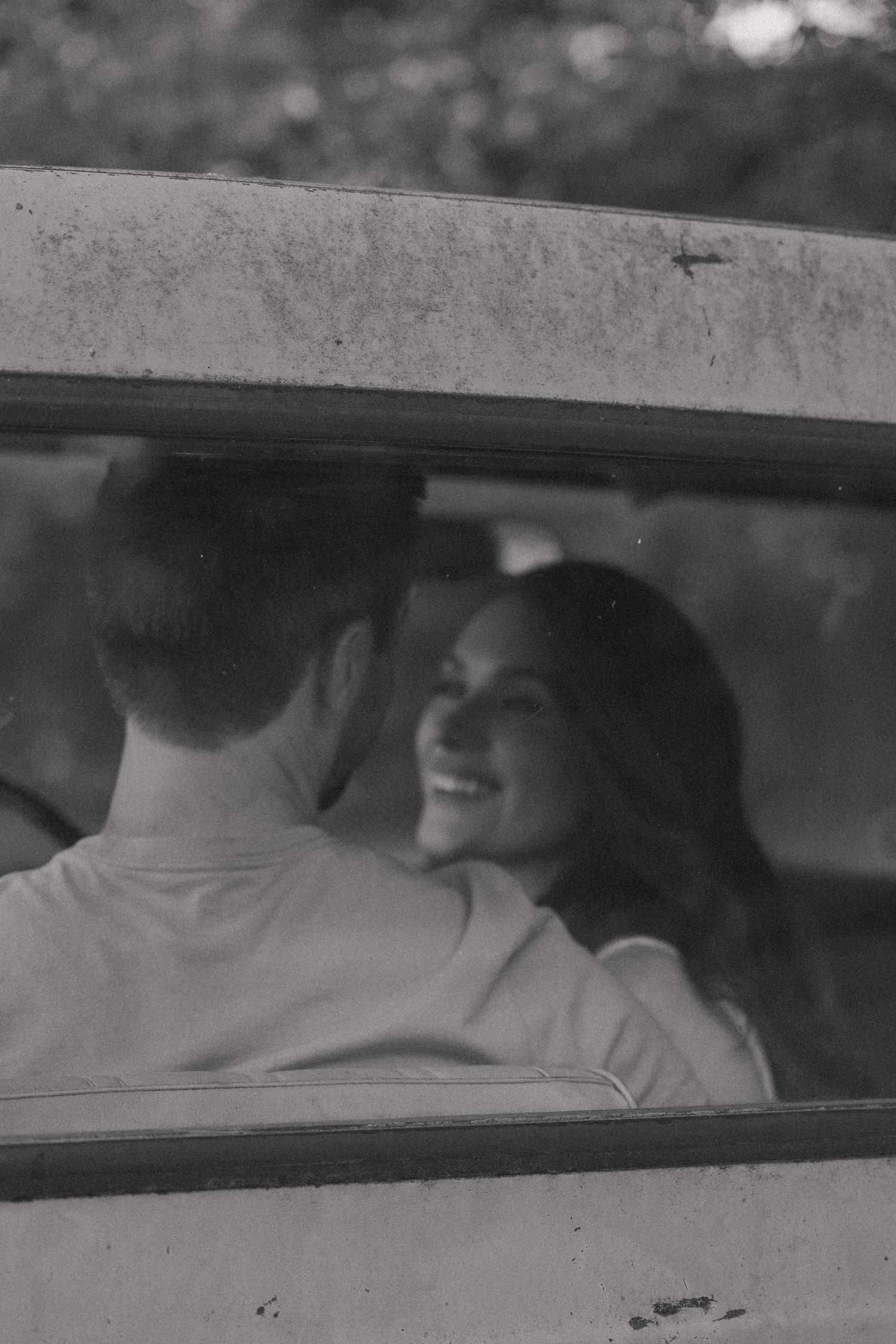 Black and white photo of smiling couple seen through vintage truck window.
