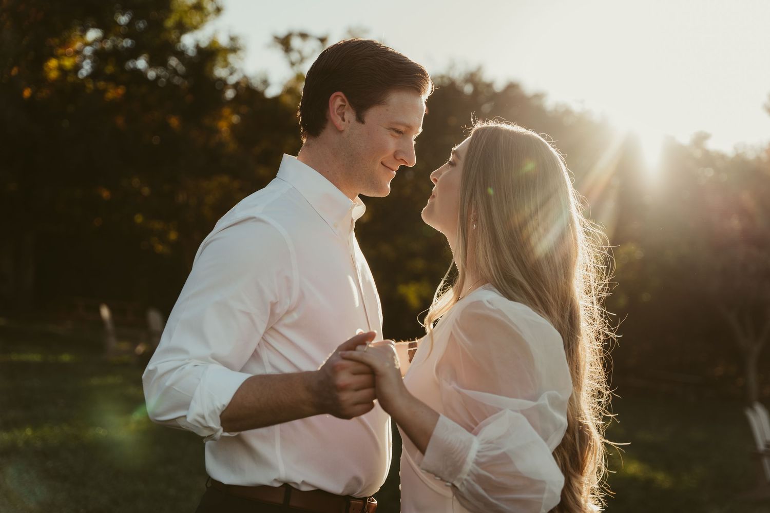 Couple sharing a romantic moment with golden sunlight glowing behind them outdoors.