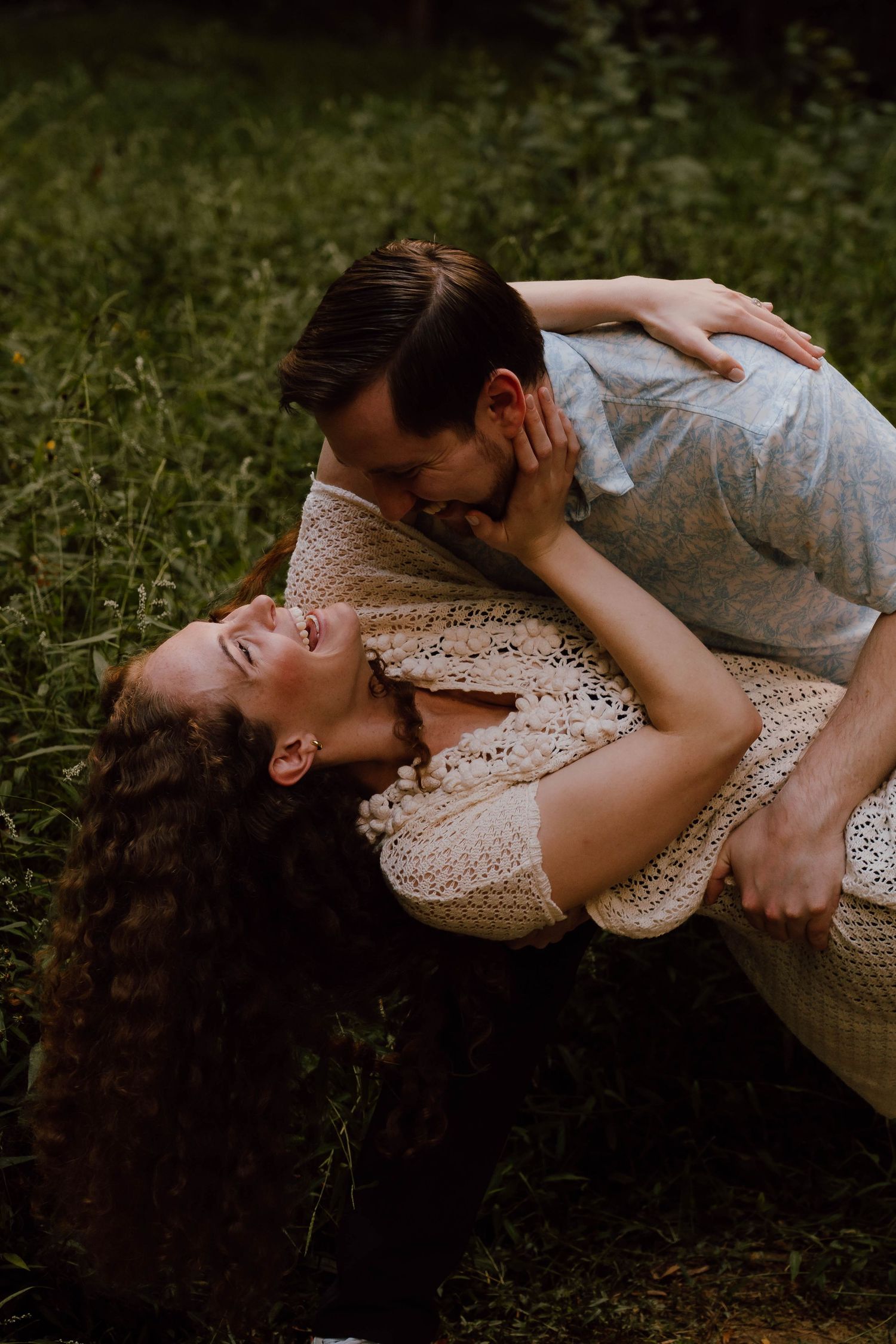 Couple sharing a romantic moment on grass, woman laughing as man leans in for a kiss.