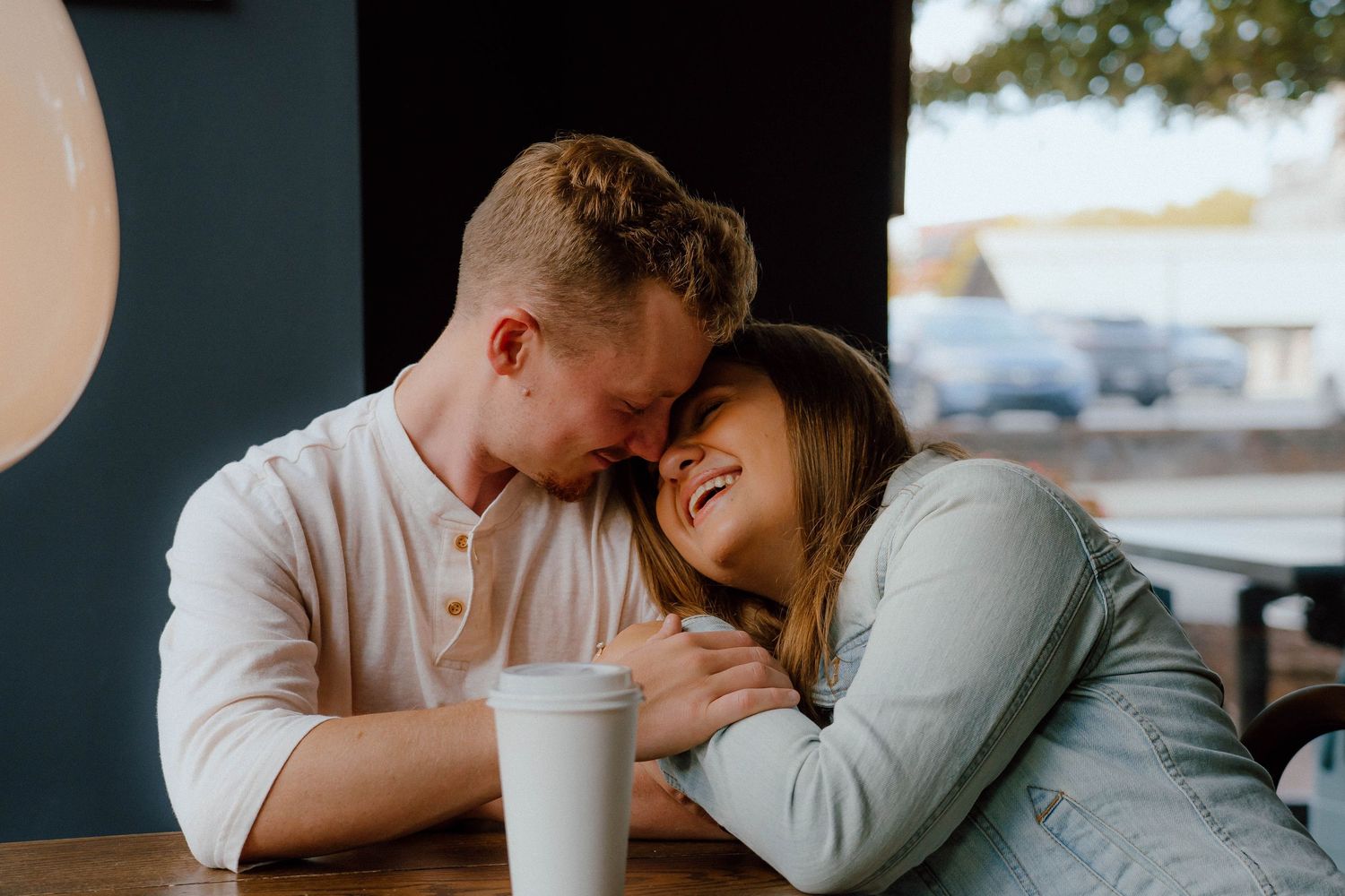 Couple sharing an intimate moment at a cafe table, laughing and leaning close together.