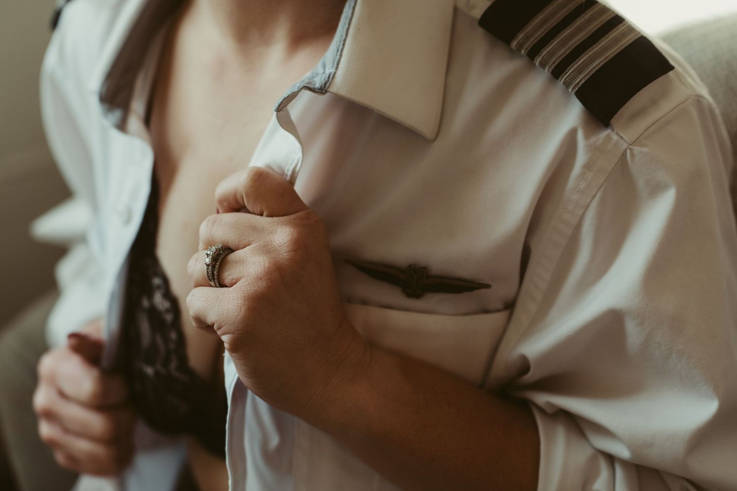 Close-up of a woman opening a white pilot shirt revealing black lace lingerie beneath.
