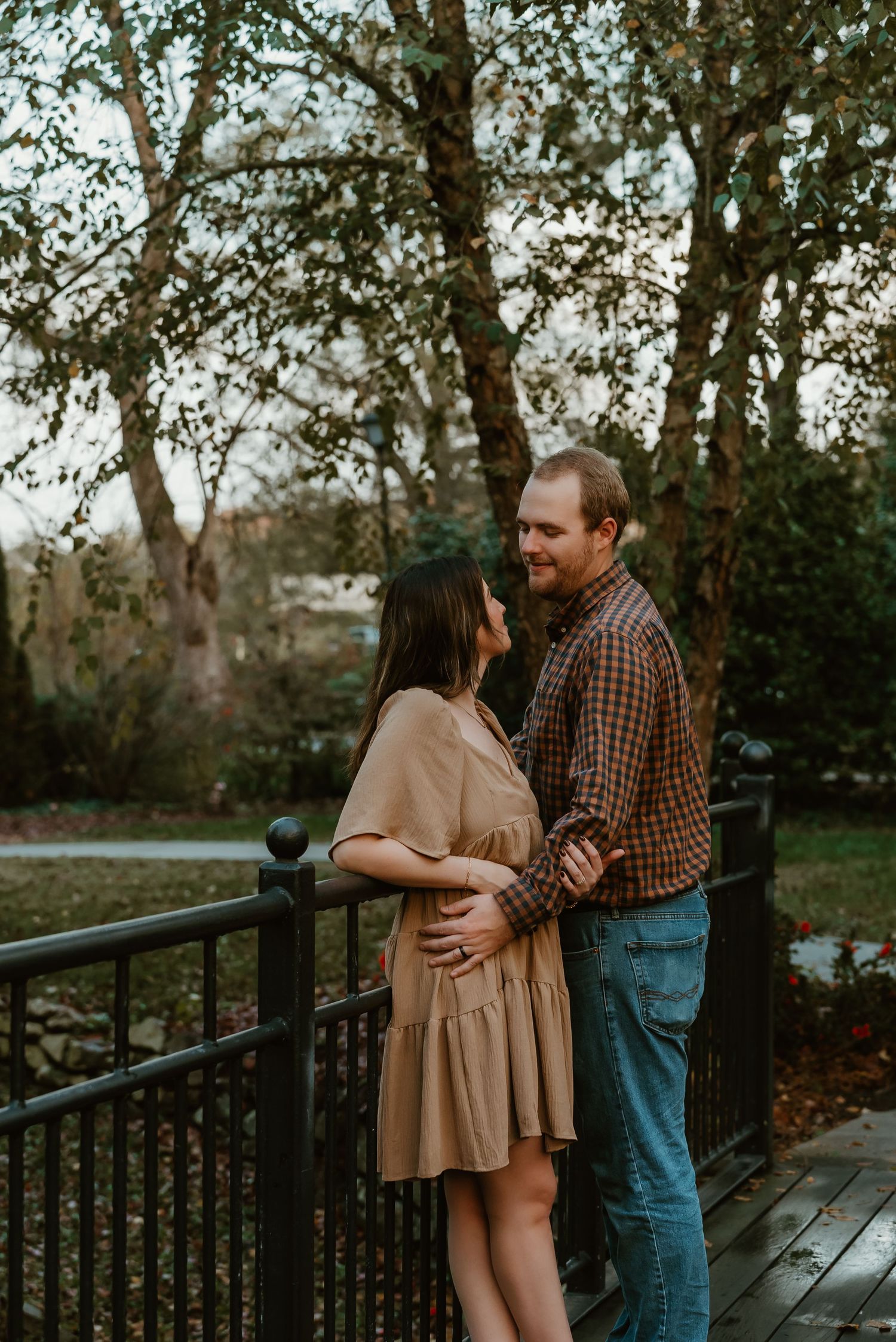 Couple embracing on a wooden bridge railing surrounded by autumn trees.