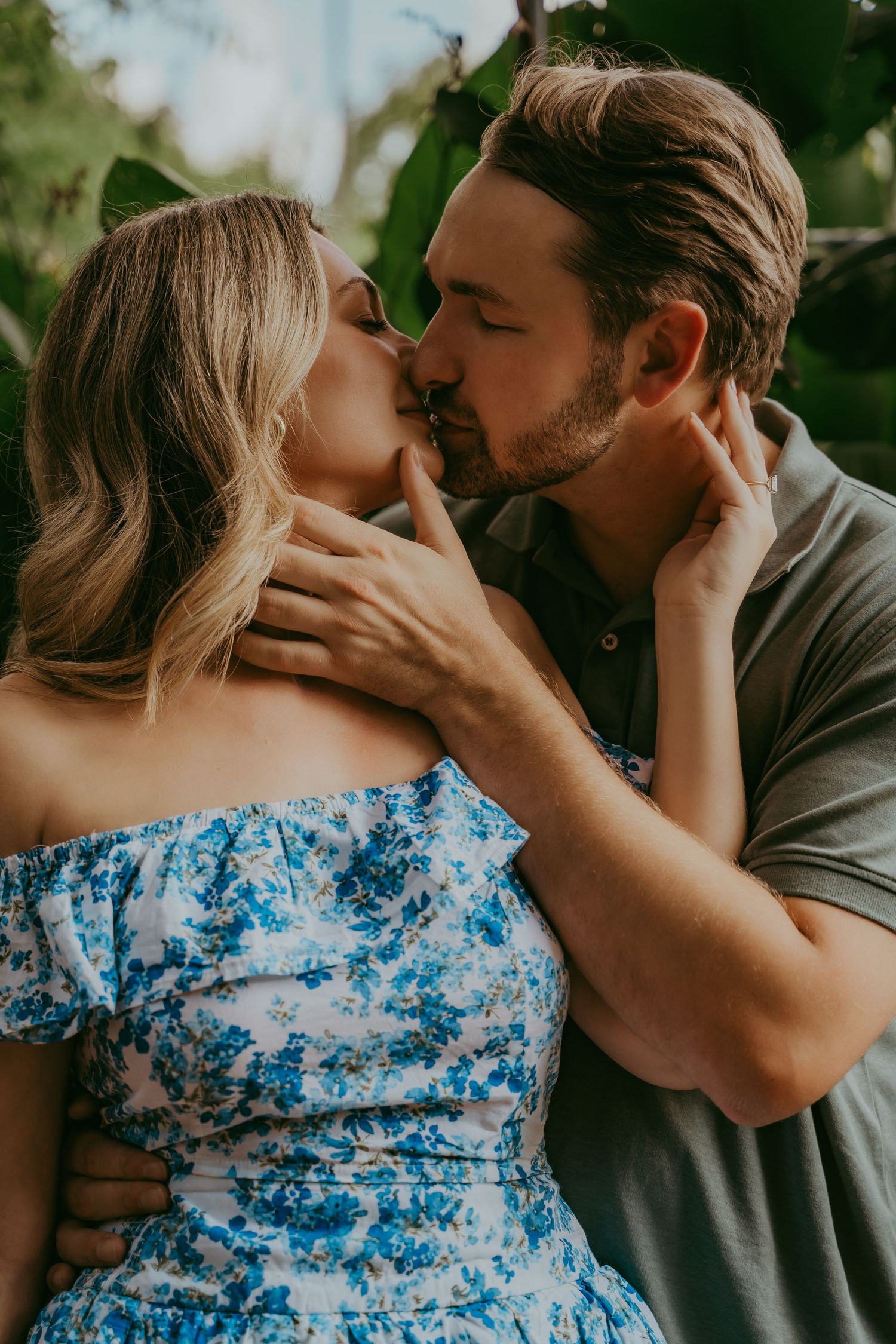 Couple sharing a romantic kiss, woman in blue floral off-shoulder dress outdoors.