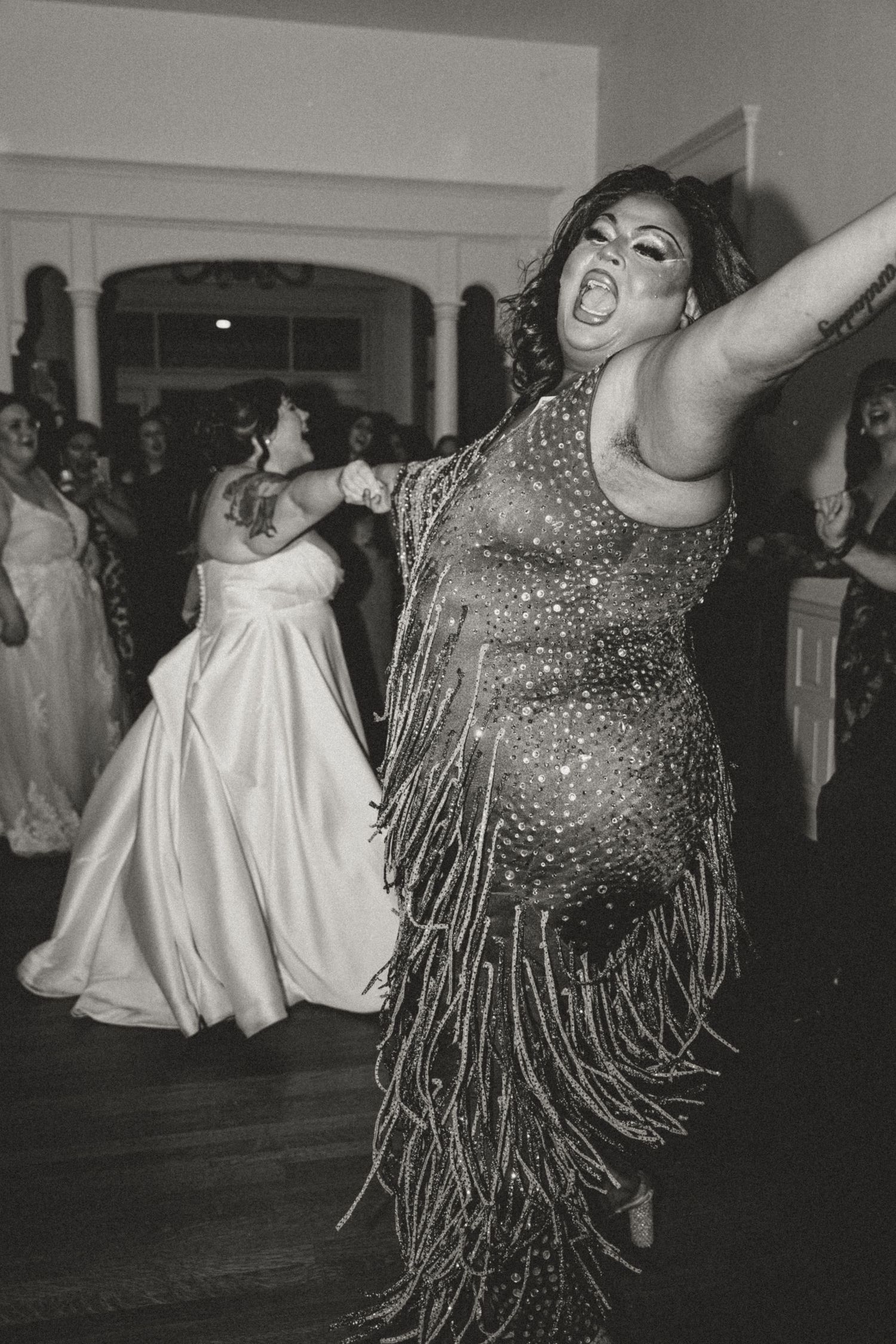 Performer in sparkling fringe dress dances energetically in black and white photo at wedding reception.
