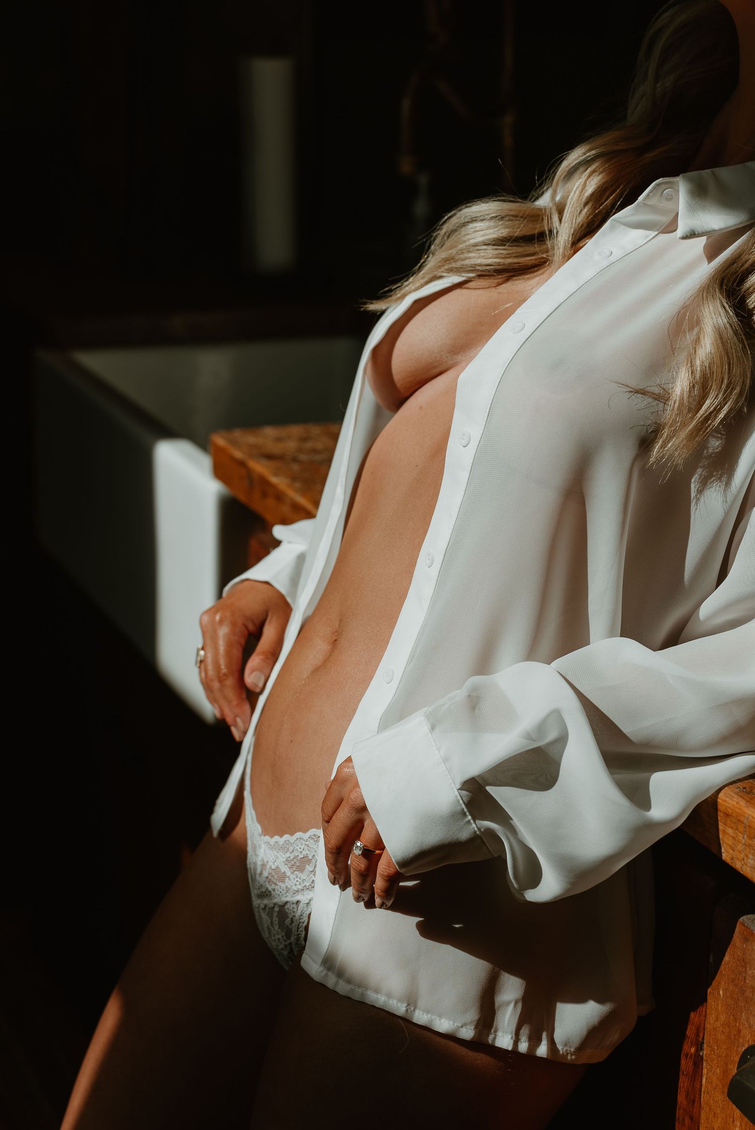 Woman in open white button-down shirt and lace lingerie posing in moody dark studio boudoir photography.
