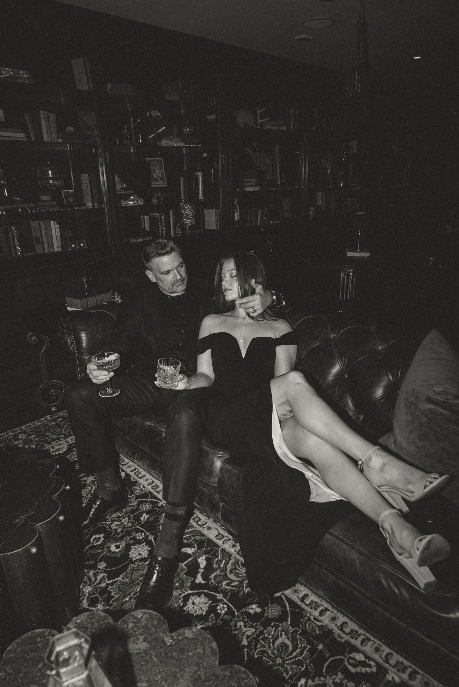 Elegant black and white photo of a couple relaxing on leather sofa in a dark sophisticated library.