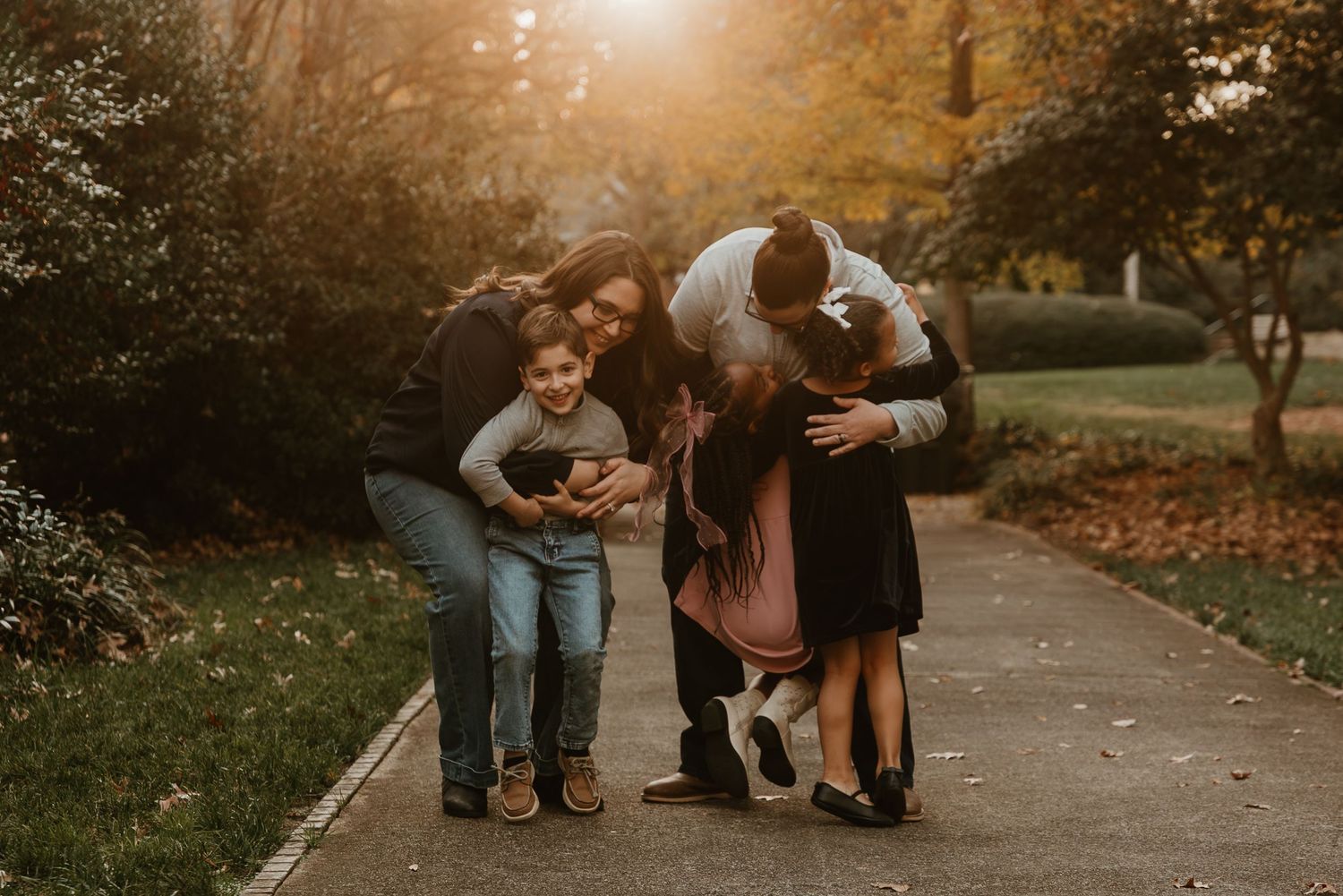 Joyful family of five sharing hugs and laughter on a tree-lined path during autumn.
