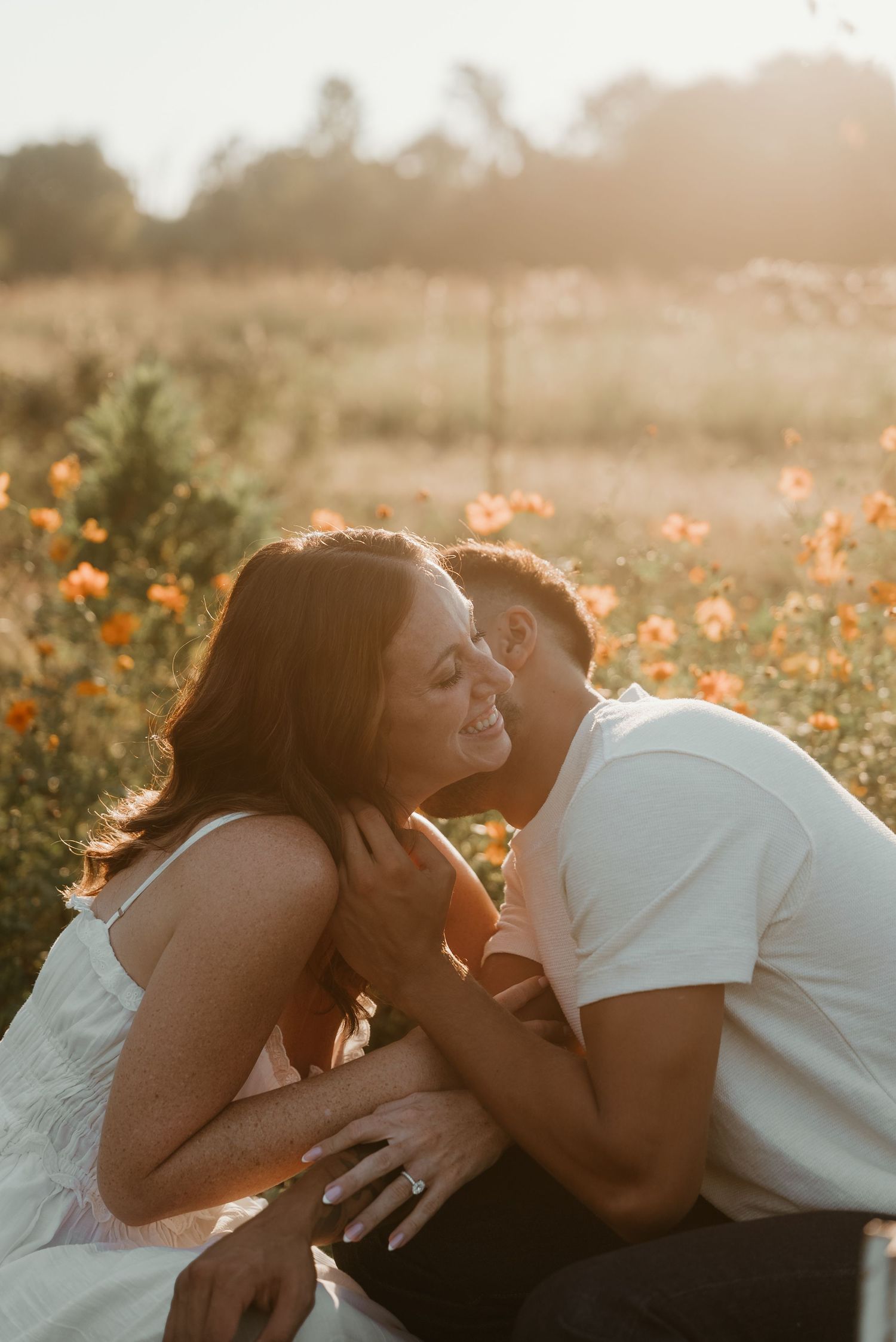 Couple sharing a tender kiss in a sunlit flower field during golden hour engagement session.