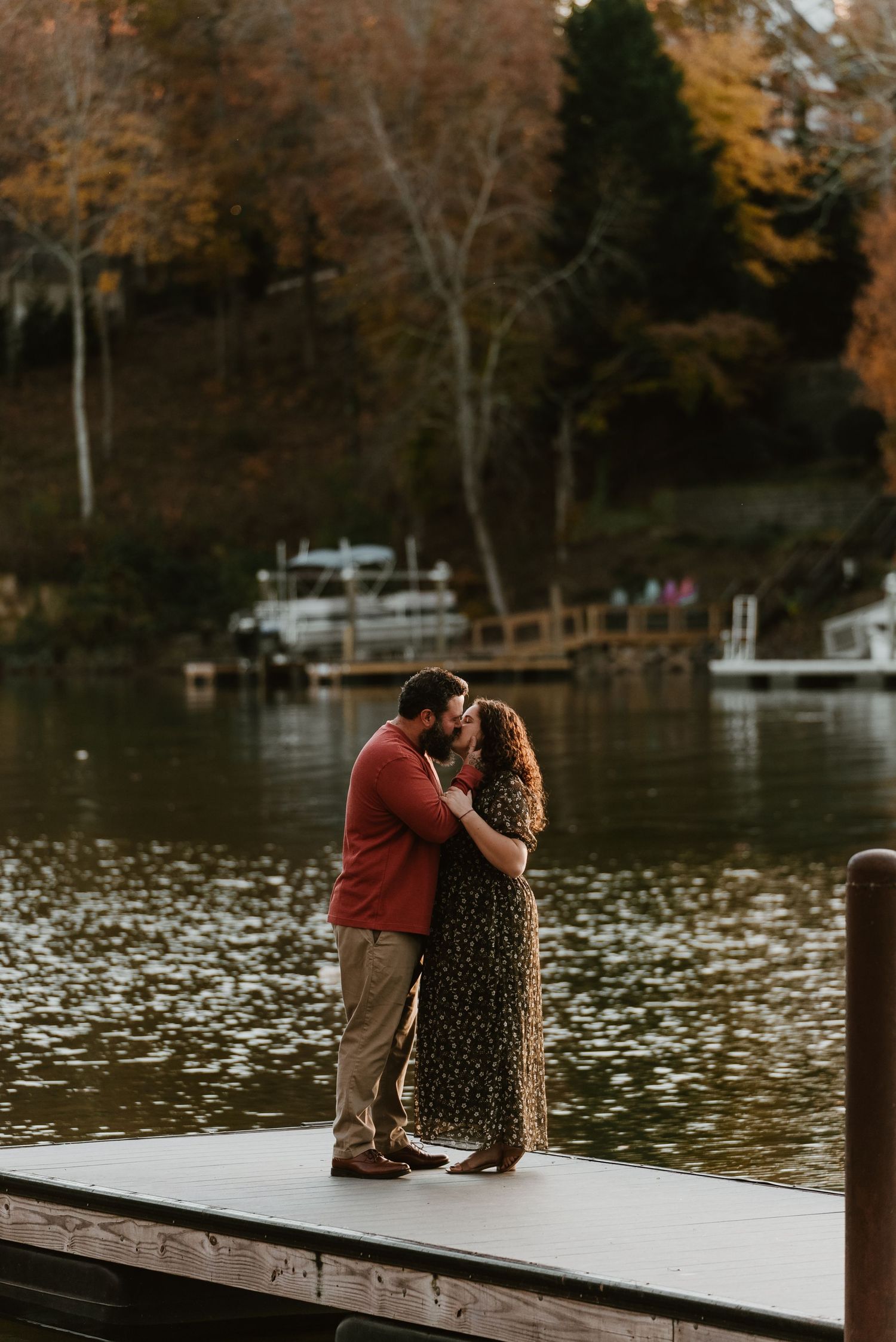 Couple kissing on a lakeside dock surrounded by colorful autumn foliage.