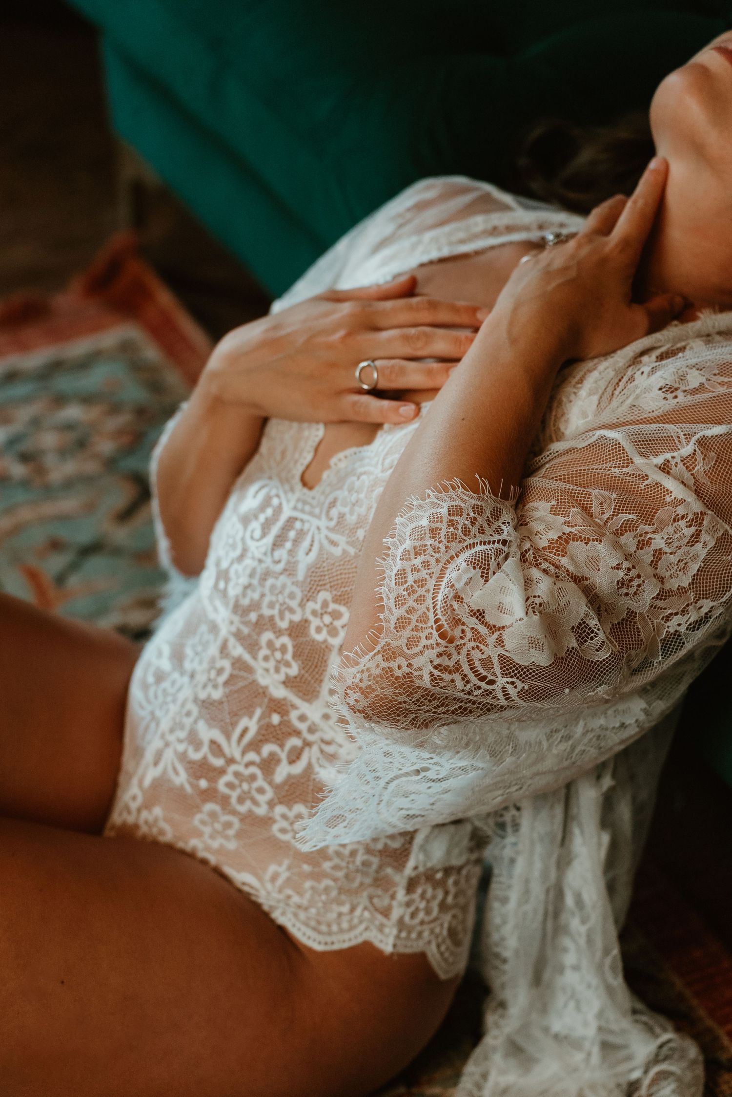 Woman in sheer white lace robe sitting on floor touching chest.