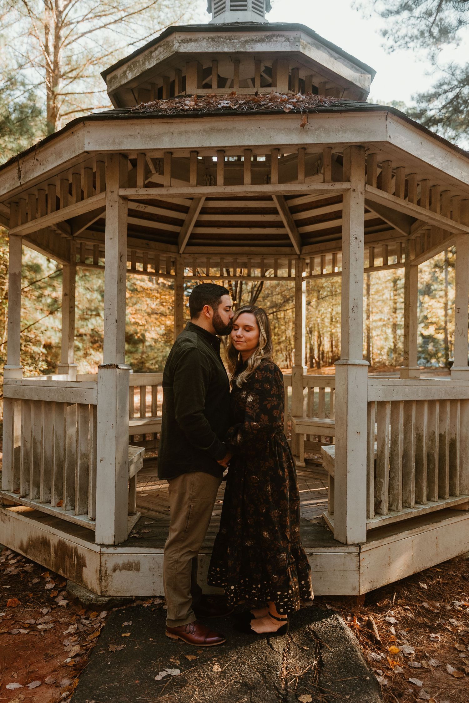 Couple sharing a romantic moment in front of a rustic wooden gazebo during autumn.