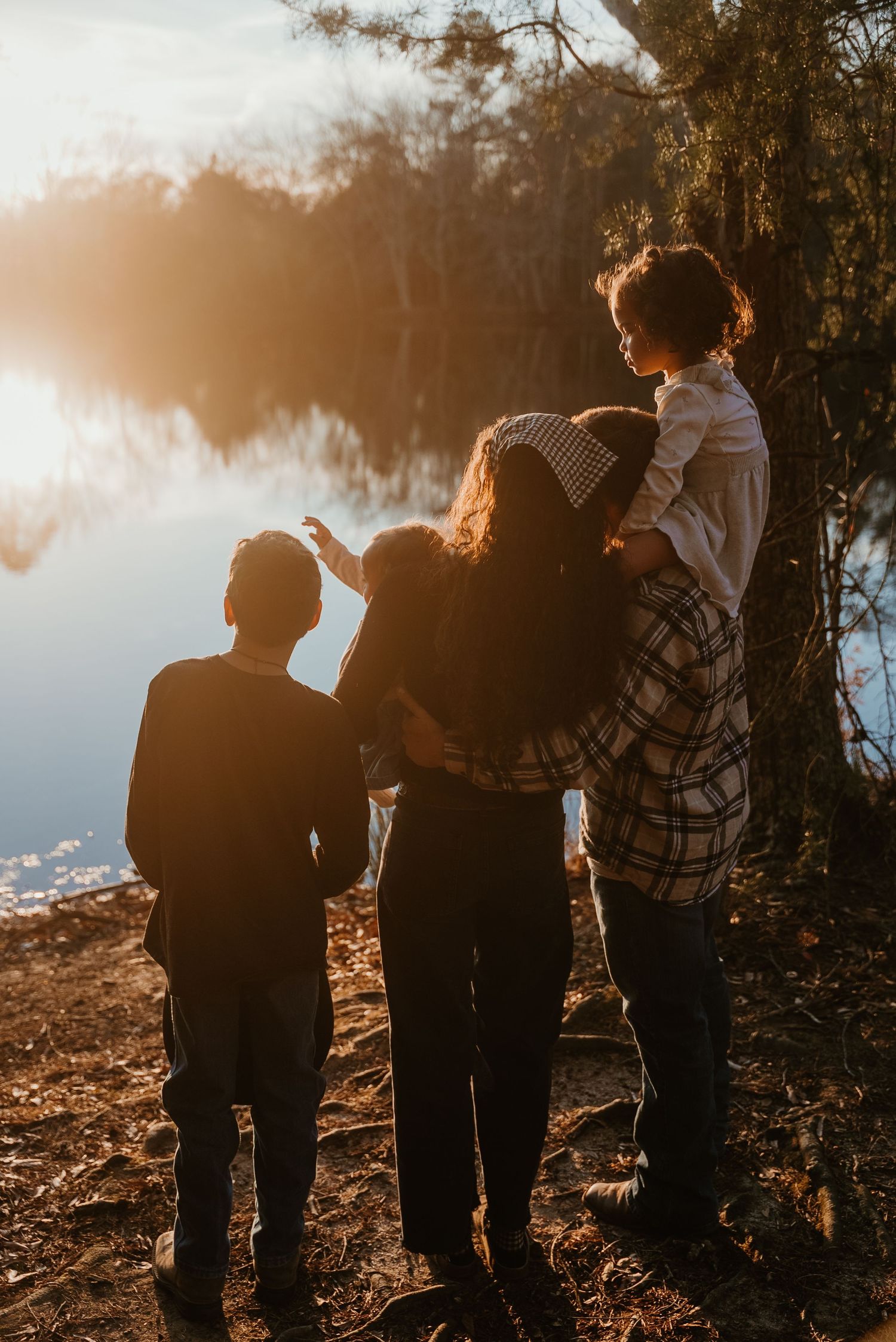 Family of four standing by a tranquil lake at golden hour, children pointing at the glowing sunset reflection.