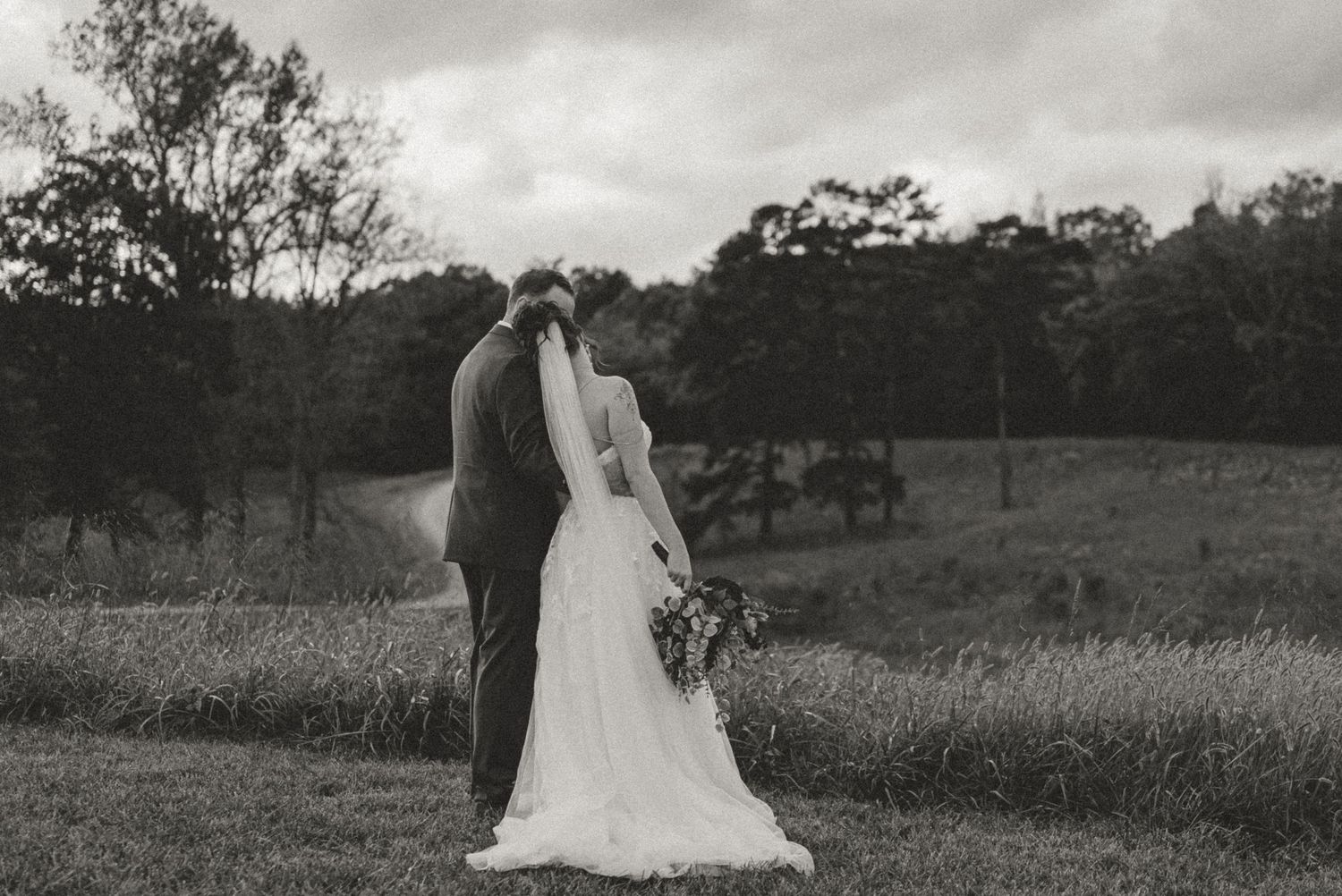Black and white romantic photo of a bride and groom kissing in a scenic countryside setting.
