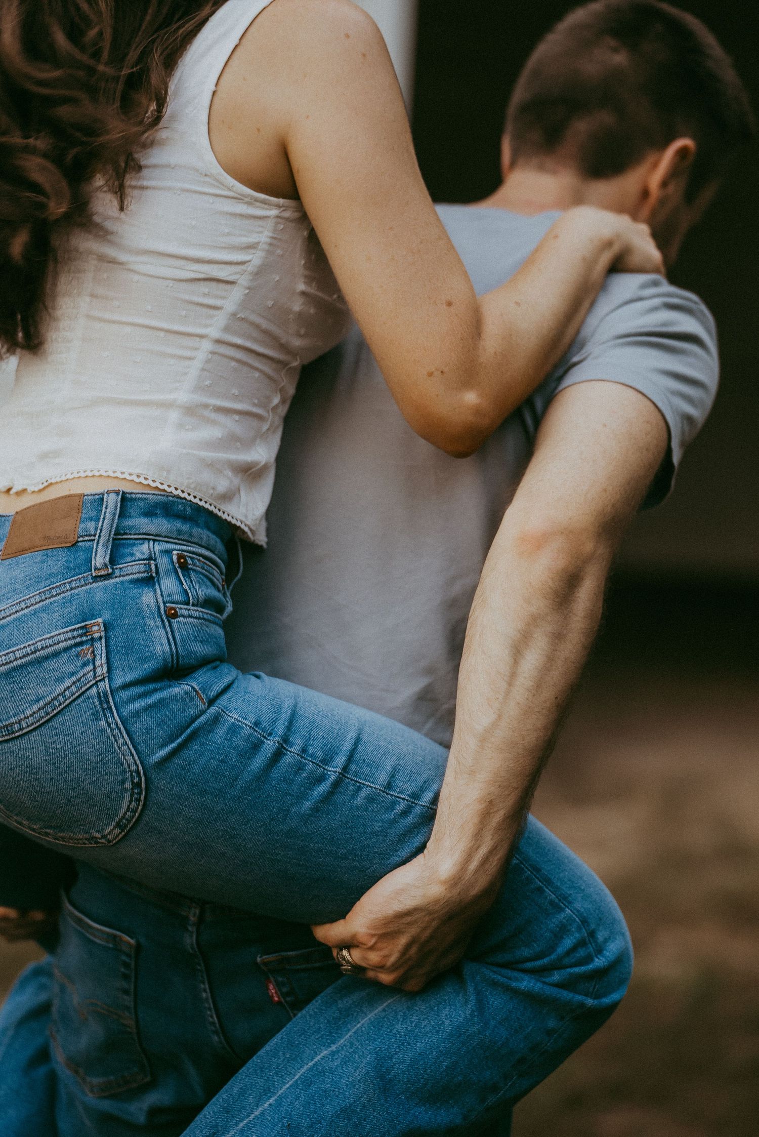 Close-up of couple embracing showing woman in white tank top and blue Levis jeans outdoors.
