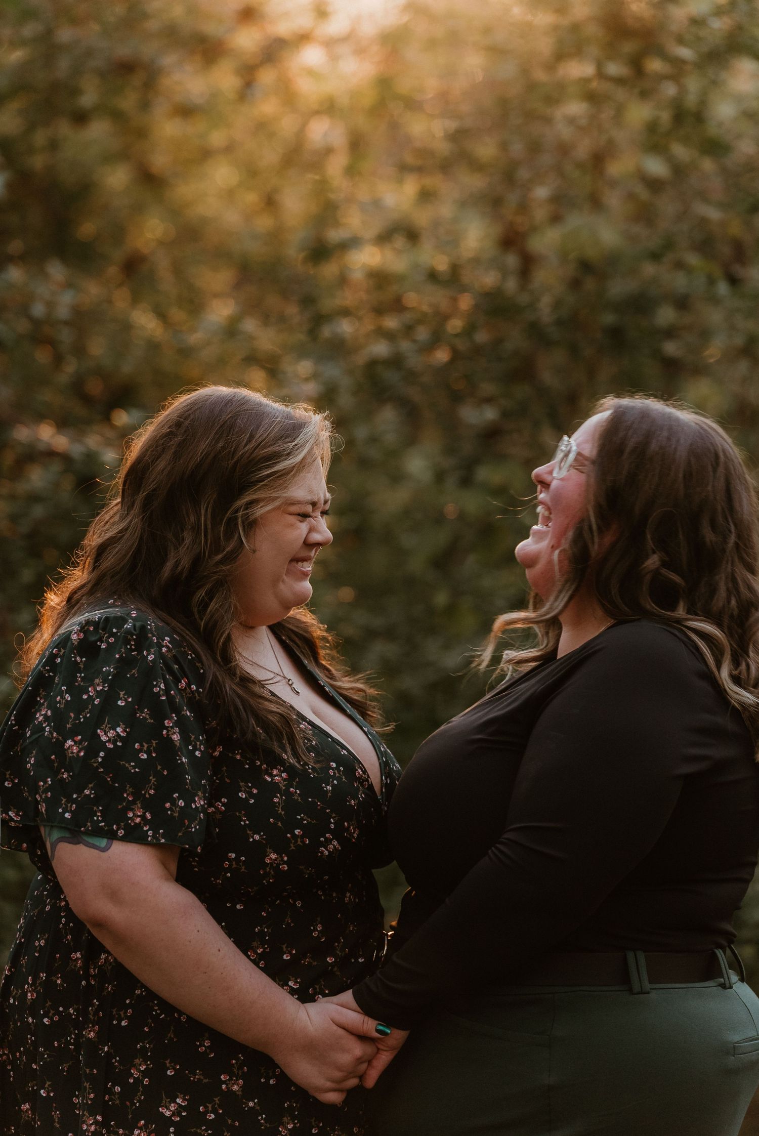 Two women holding hands and smiling at each other in warm golden backlit outdoor setting.