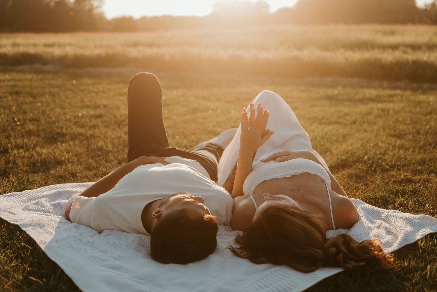 Couple lying on a white blanket in an open field during a golden sunset engagement shoot.