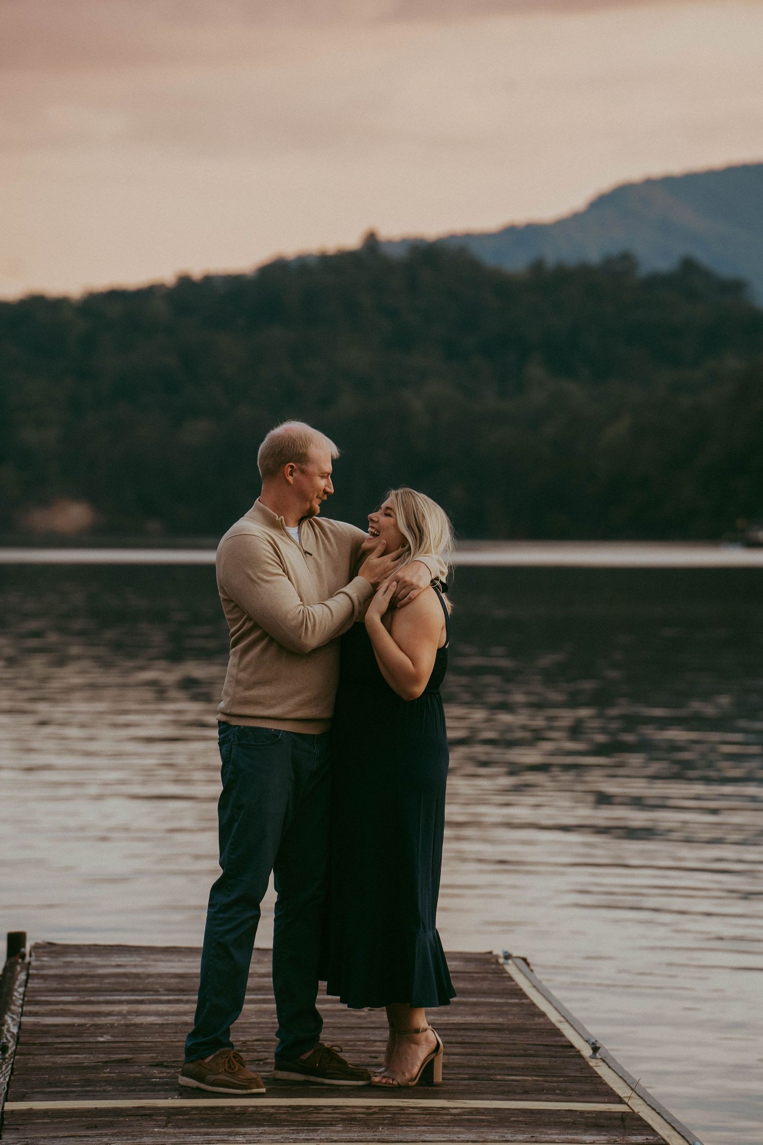 Couple dancing romantically on a wooden dock at sunset with a calm mountain lake behind.