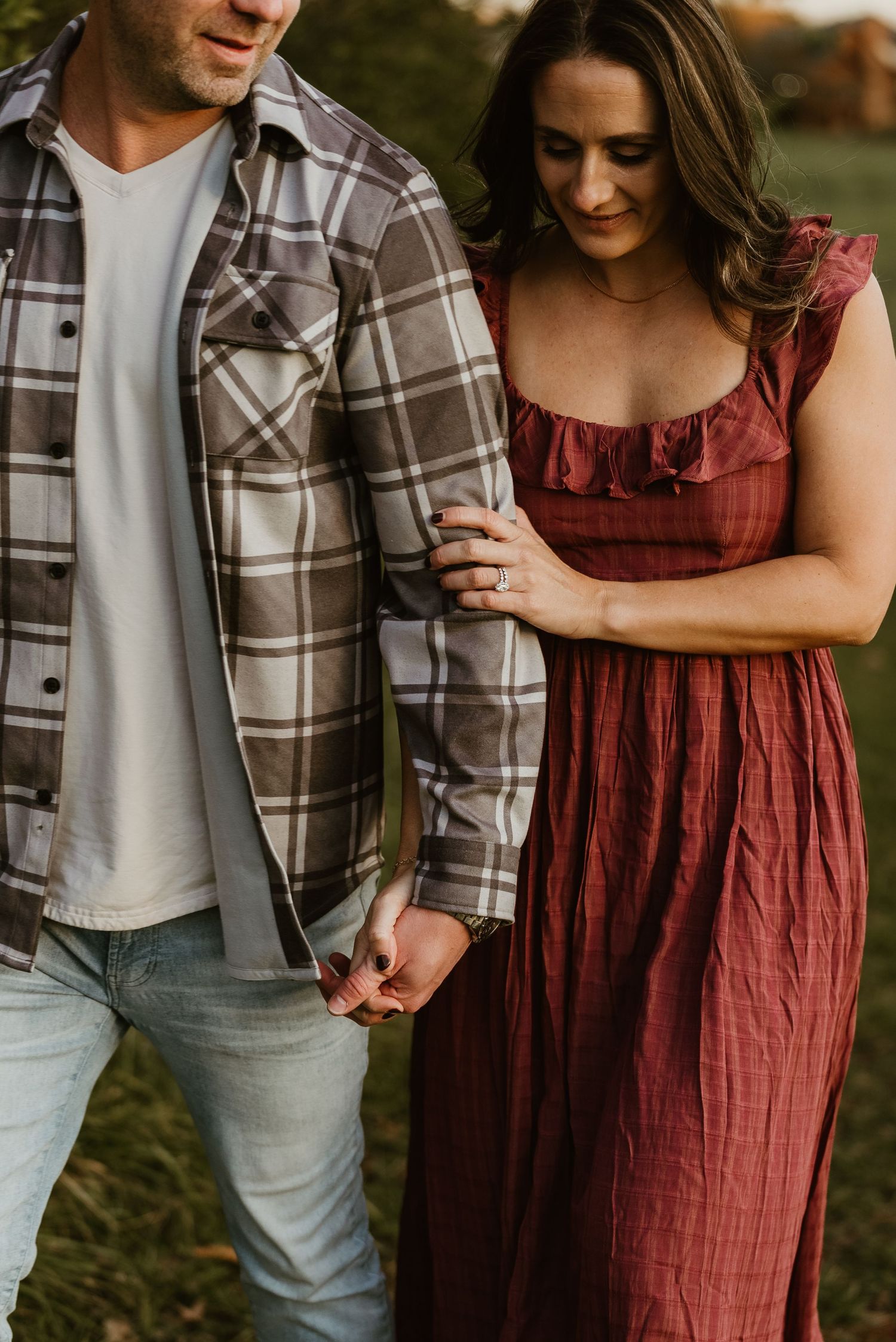 Close-up of couple holding hands while walking, woman in burgundy dress and man in plaid shirt.