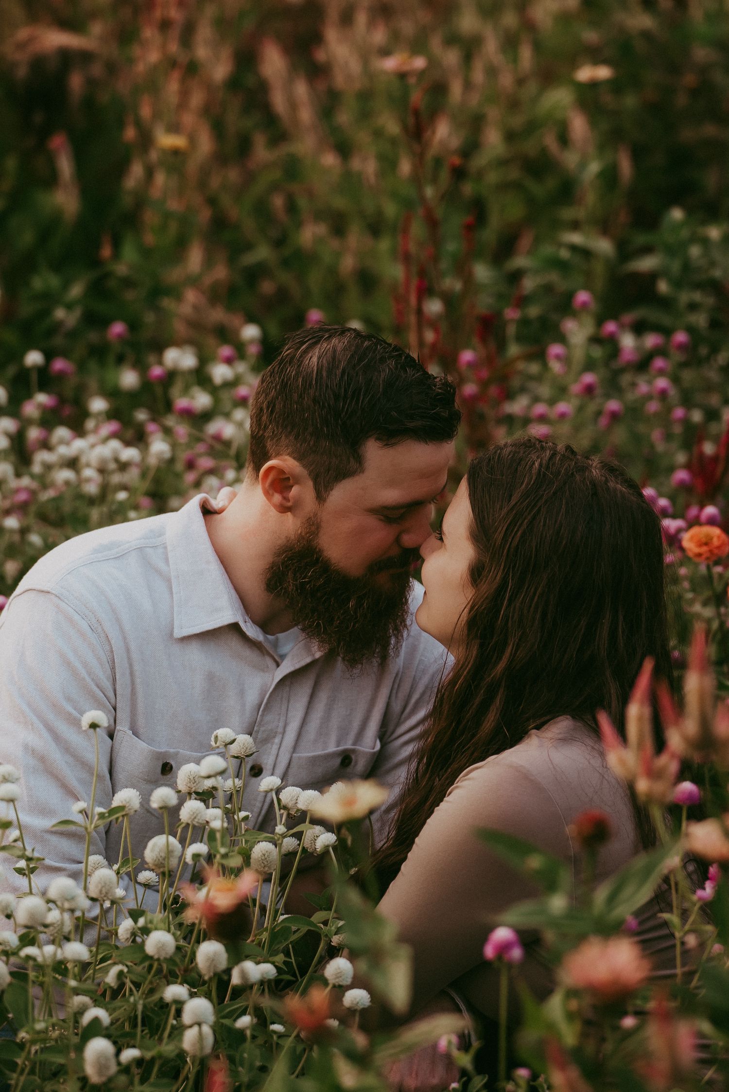 Bearded man and brunette woman sharing a kiss in a colorful wildflower garden.