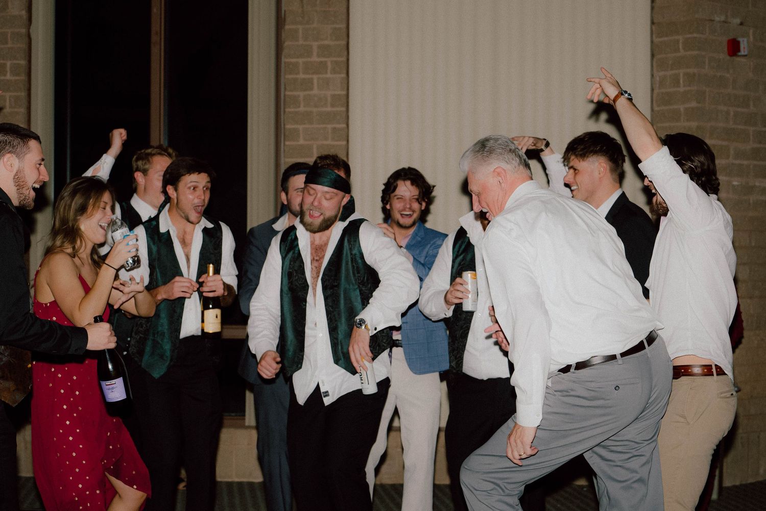 Wedding reception guests dancing and celebrating with drinks at lively indoor party.